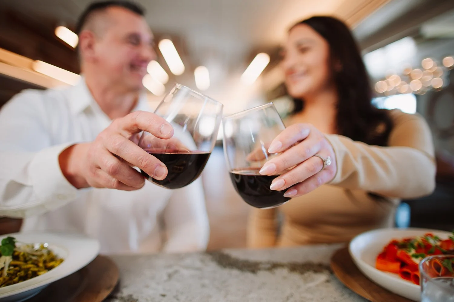 a couple cheers their red wine glasses