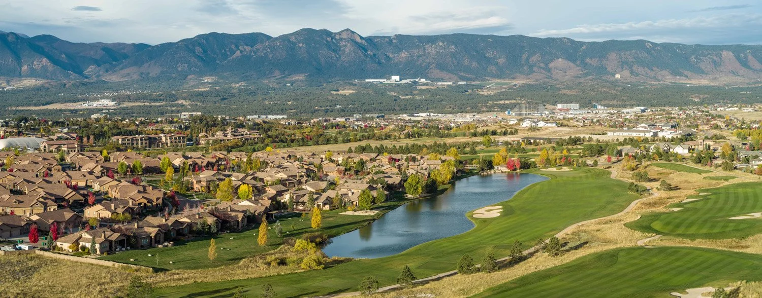 A scenic view of a residential neighborhood next to a golf course with a water body, with mountains in the background.