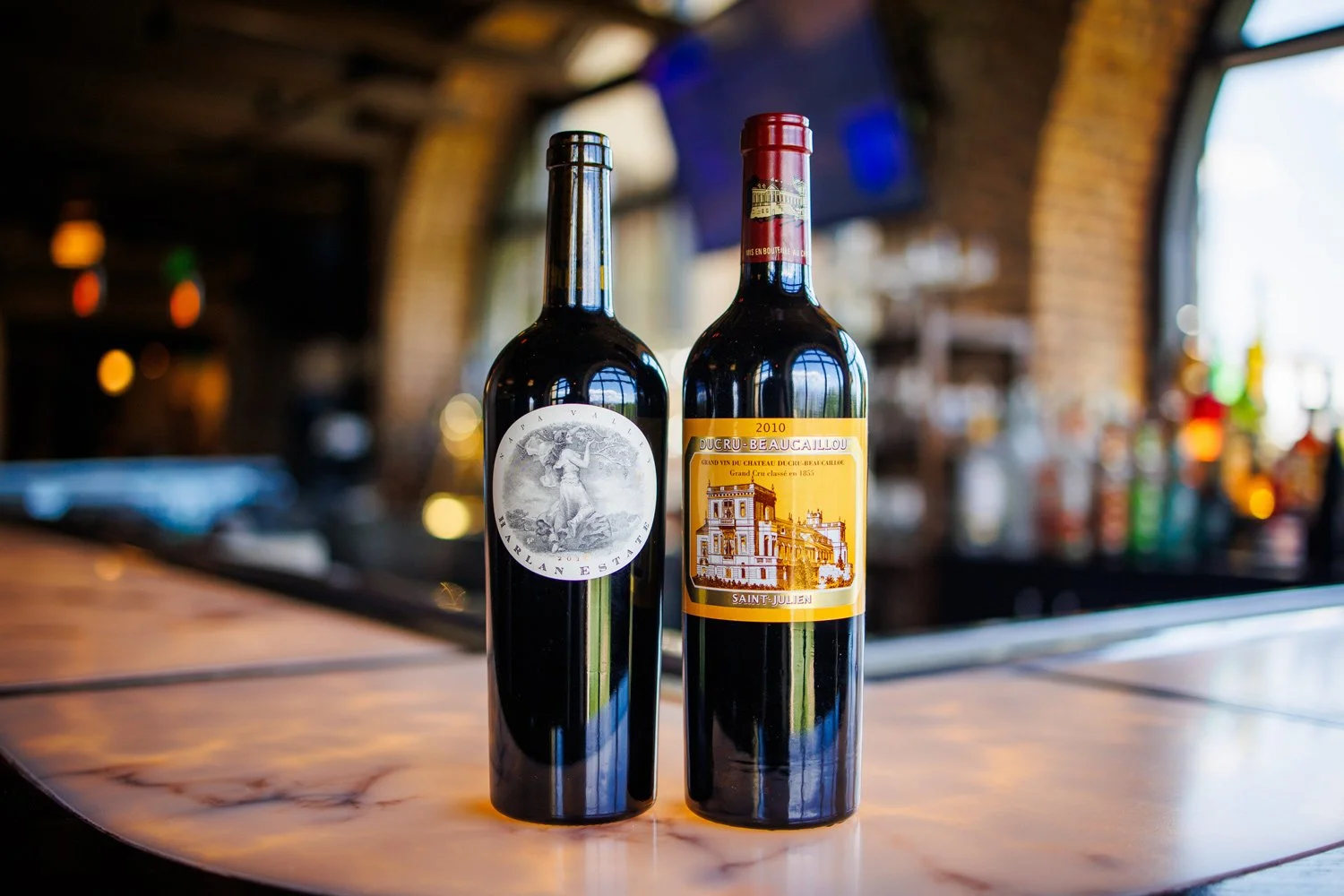 Two bottles of red wine on a bar counter with a blurred background of a bar interior.