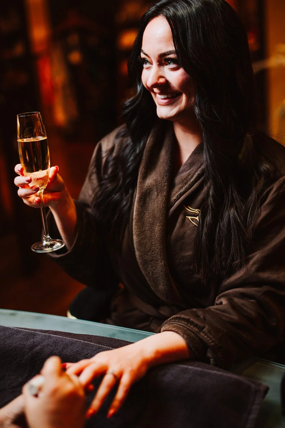 Woman in a spa robe with a glass of champagne getting her nails painted