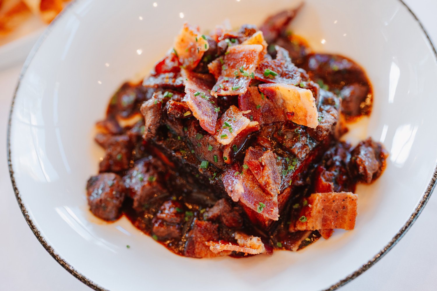A dish of beef stew with tender beef chunks in a rich, dark sauce, garnished with chopped parsley, served in a white bowl.