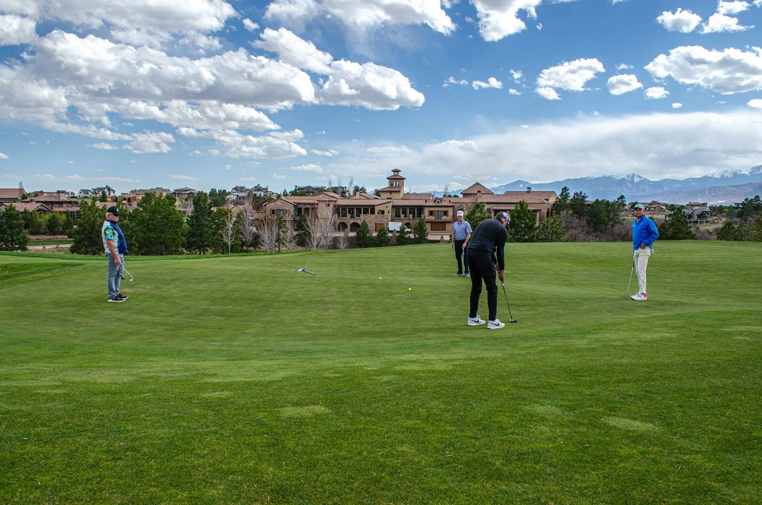 Four men playing golf on the lush Weiskopf golf course under a partly cloudy sky with mountains in the background.
