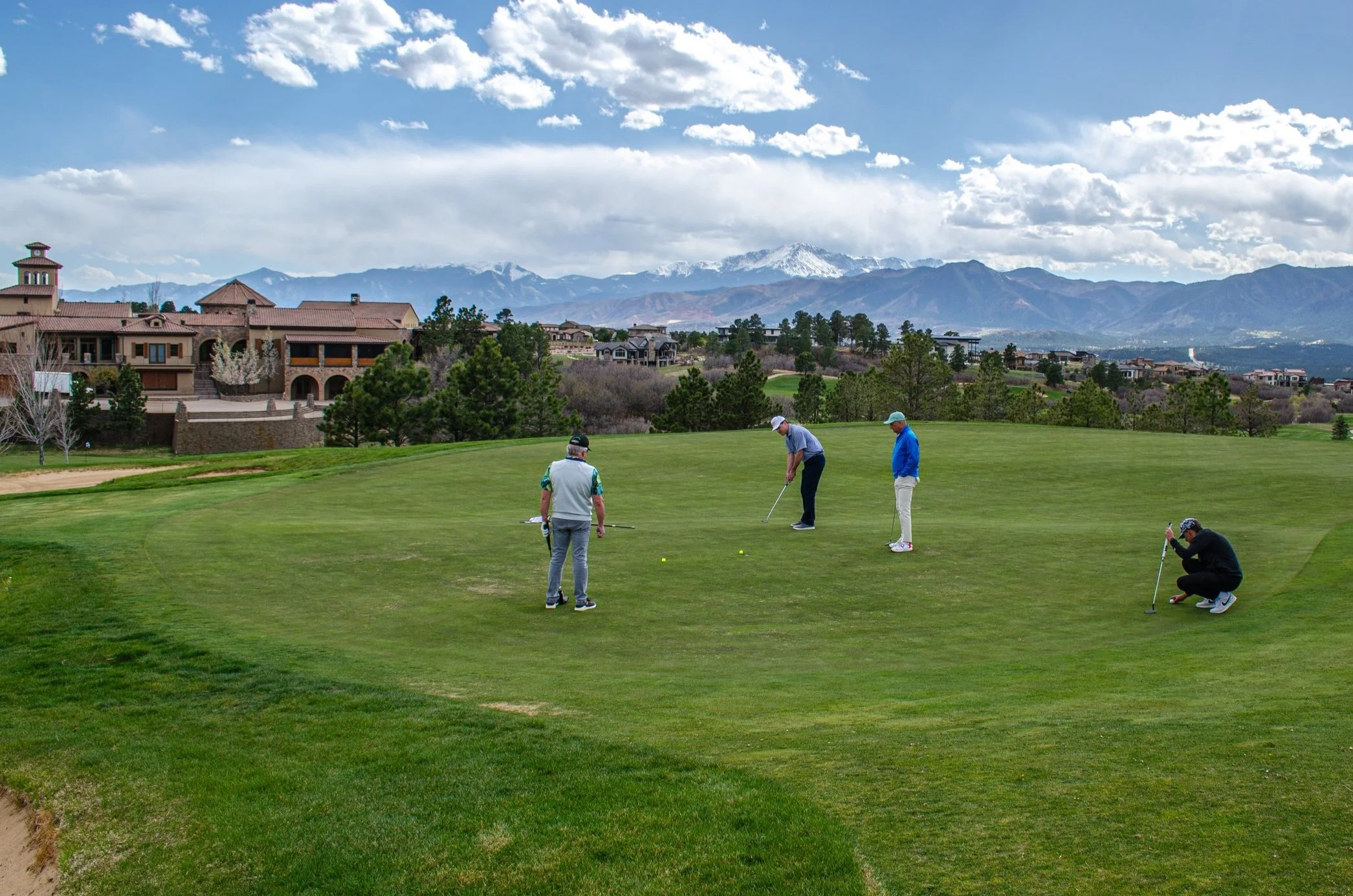 group golf lesson of three golfers on the 18th hole in front of the clubhouse with snow capped mountains in the distance
