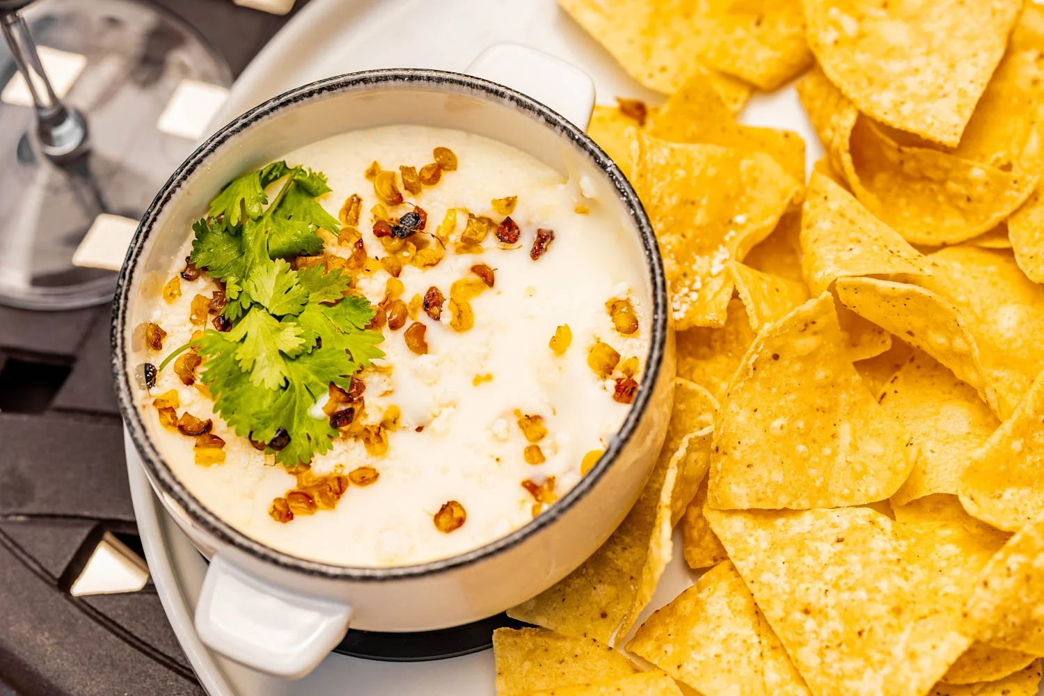 A bowl of queso dip topped with chopped peppers and cilantro, surrounded by tortilla chips.