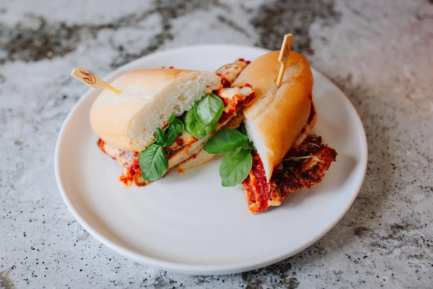 Chicken parmigiana sandwich on a white plate garnished with basil leaves
