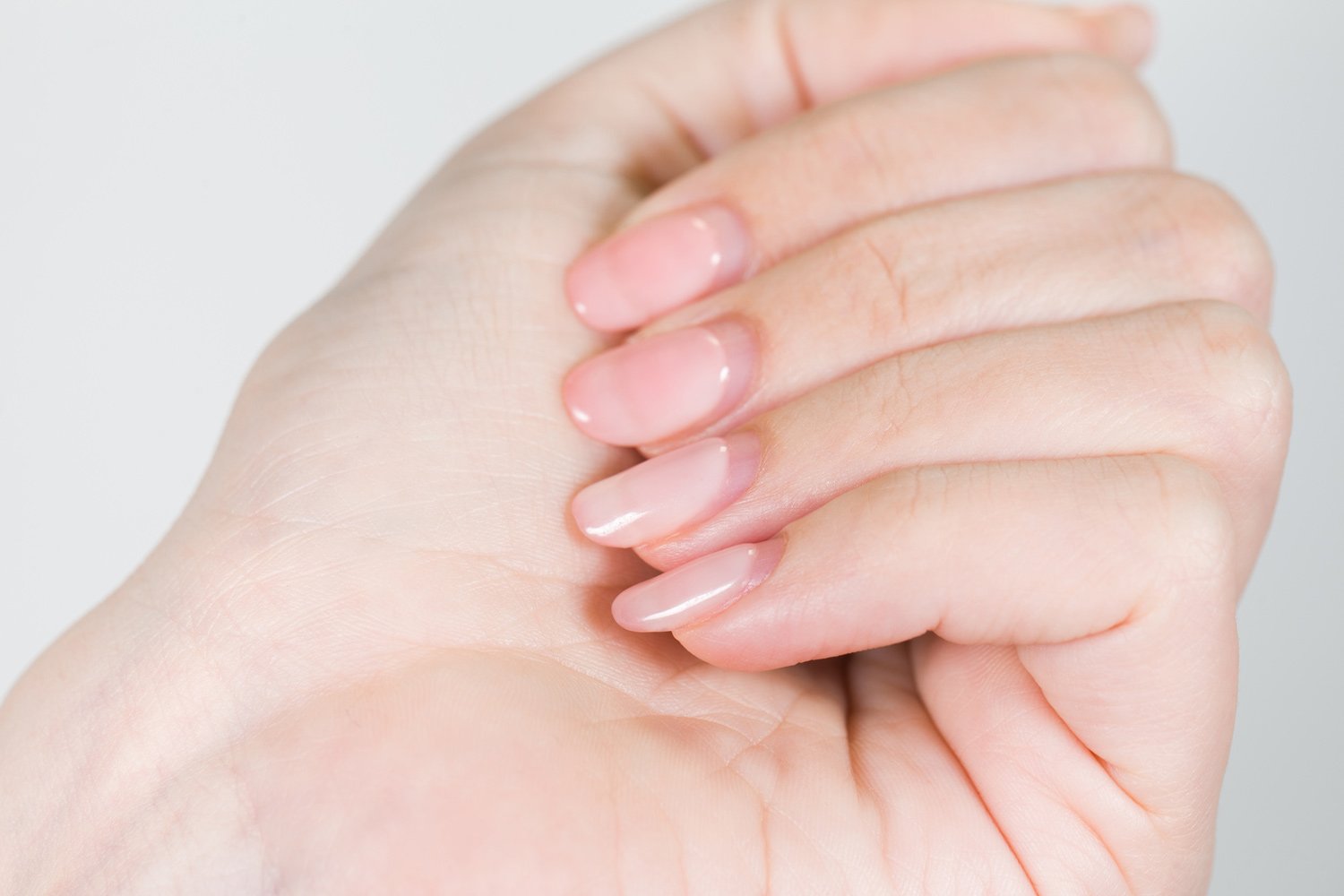 Close-up of a hand with neatly manicured, glossy light pink nails.