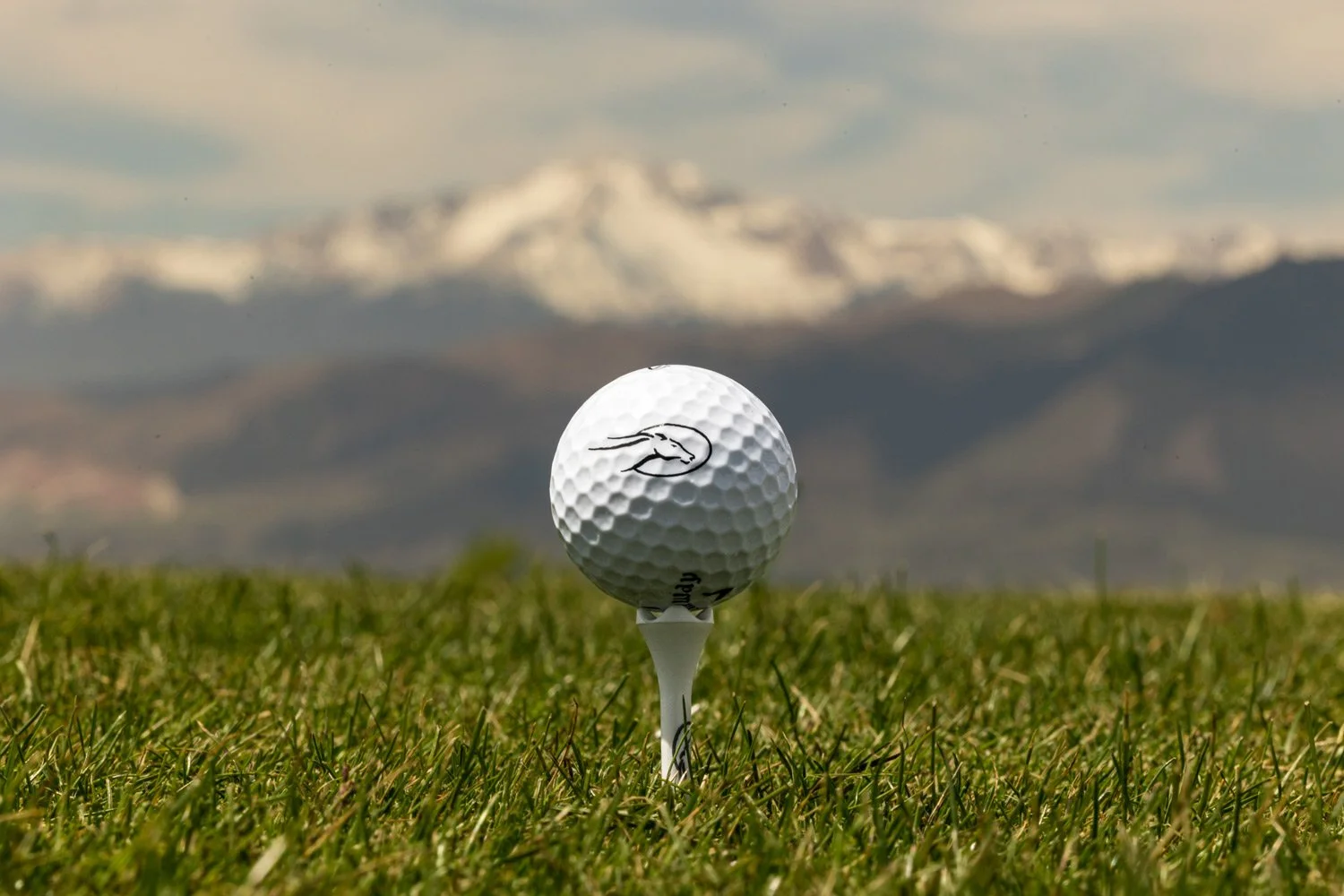 Golf ball on tee on green grass with mountainous background.