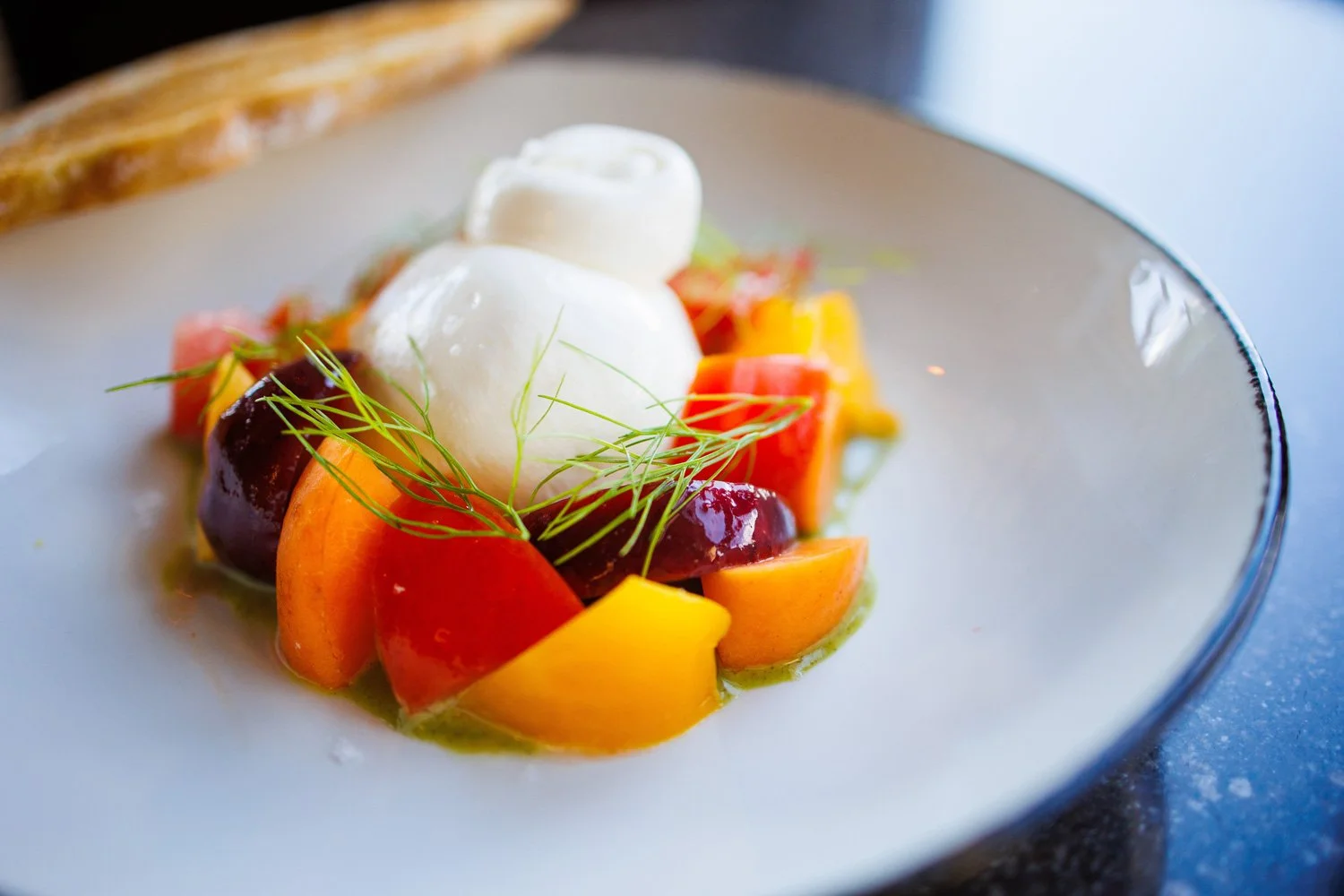 Colorful fruit salad with dollop of white cream and green garnish on a white plate.