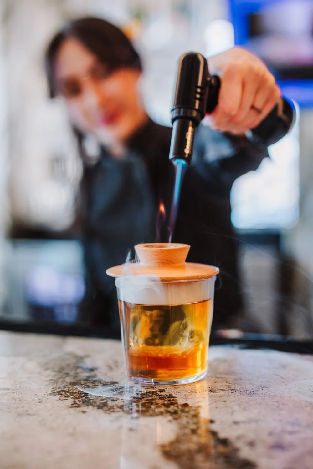A person using a culinary blowtorch to create caramelized foam on a drink.