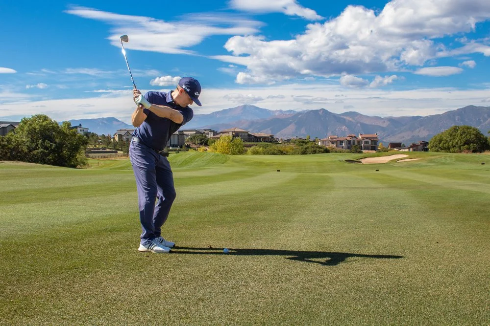 A man playing golf on a sunny golf course with mountains in the background.