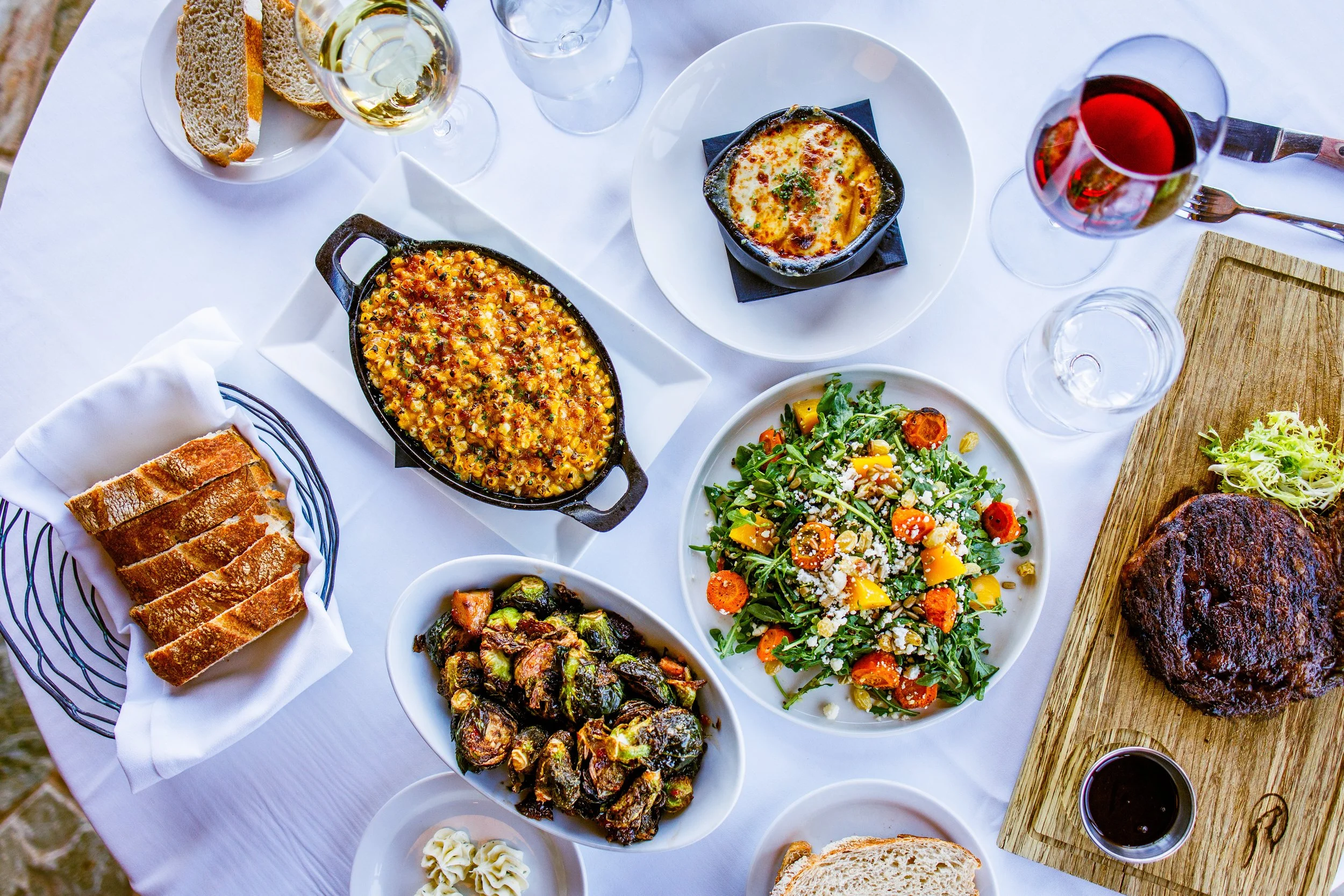 image of a fresh salad, warm slided bread, bowl of potato au grain, burssels sprouts glazed, and a prime steak