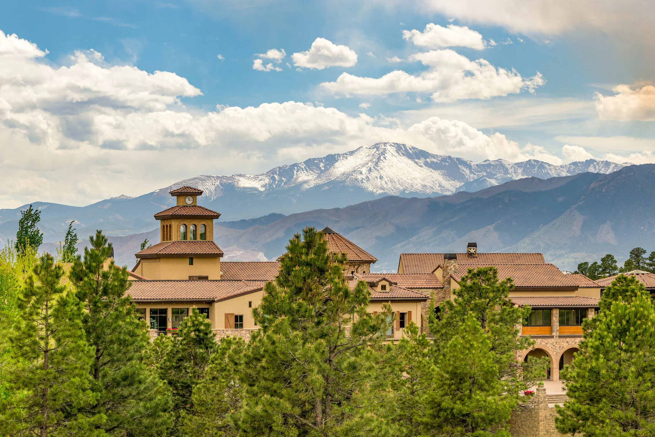 pikes peak covered with a layer of snow in the background and The Club at flying horse in the midground with pine trees in the foreground