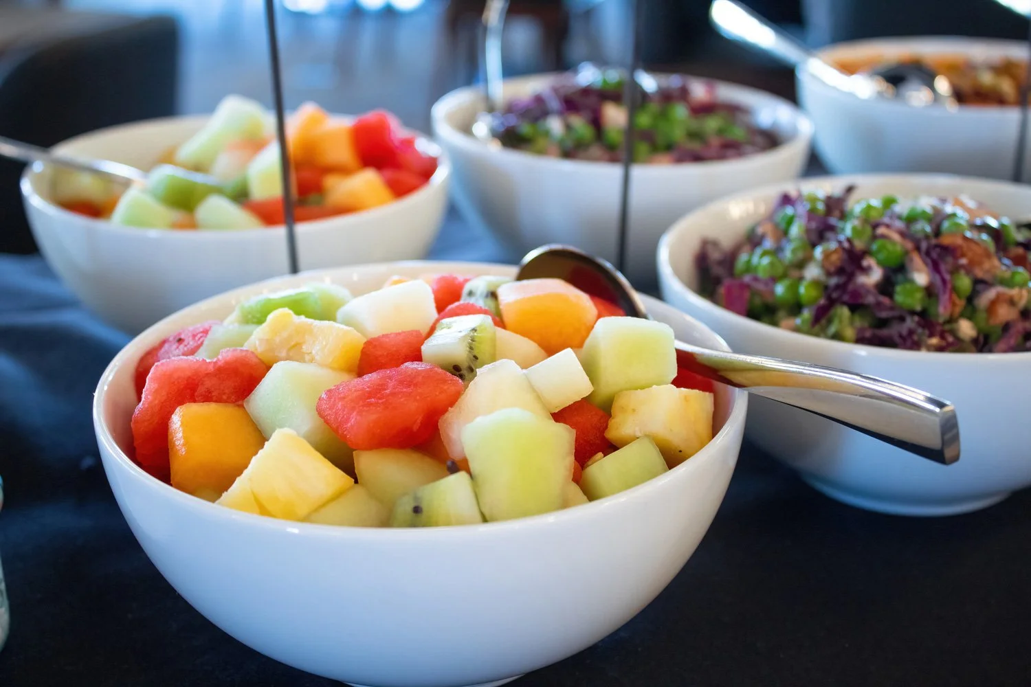 Bowls of fresh fruit salad with diced watermelon, cantaloupe, honeydew, kiwi, and melon, served at a buffet table.