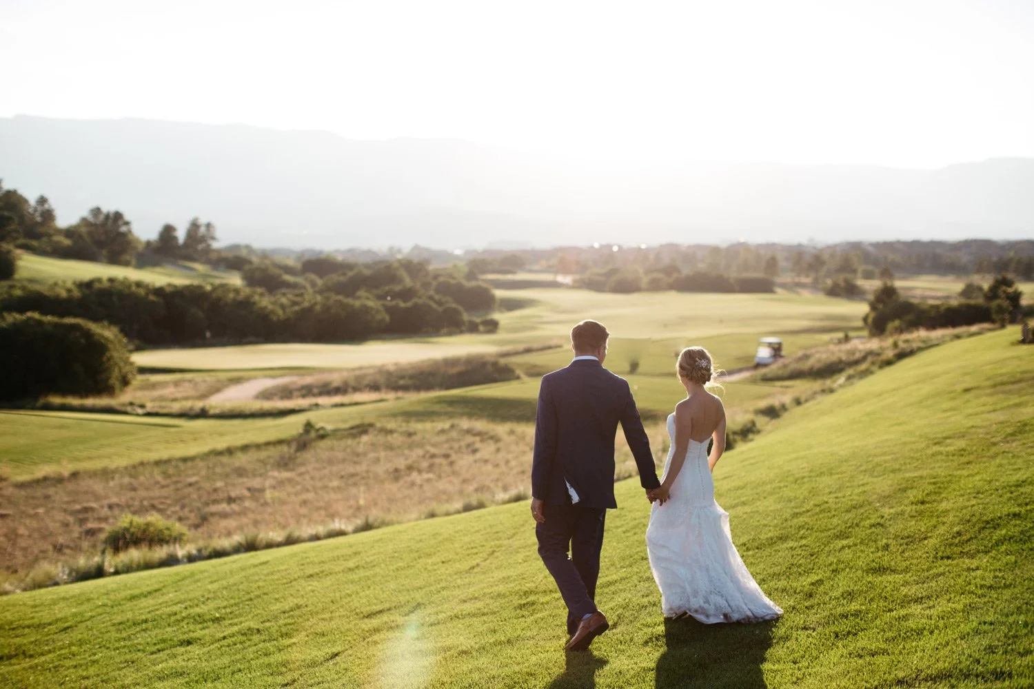 bride and groom walking into the sunset on a golf course