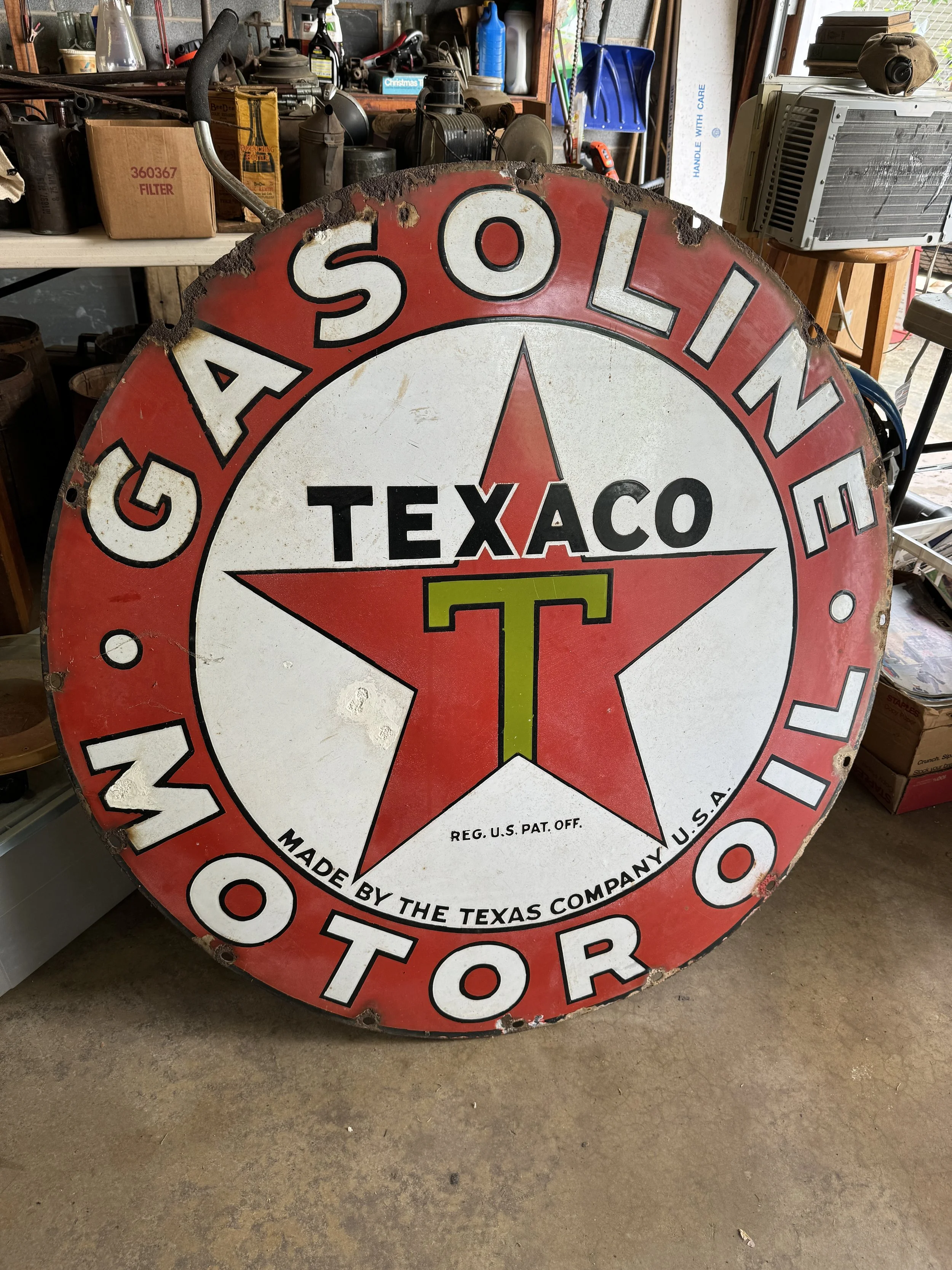 Vintage Texaco gas station sign with red star and text, showing some rust and wear, in a workshop setting.