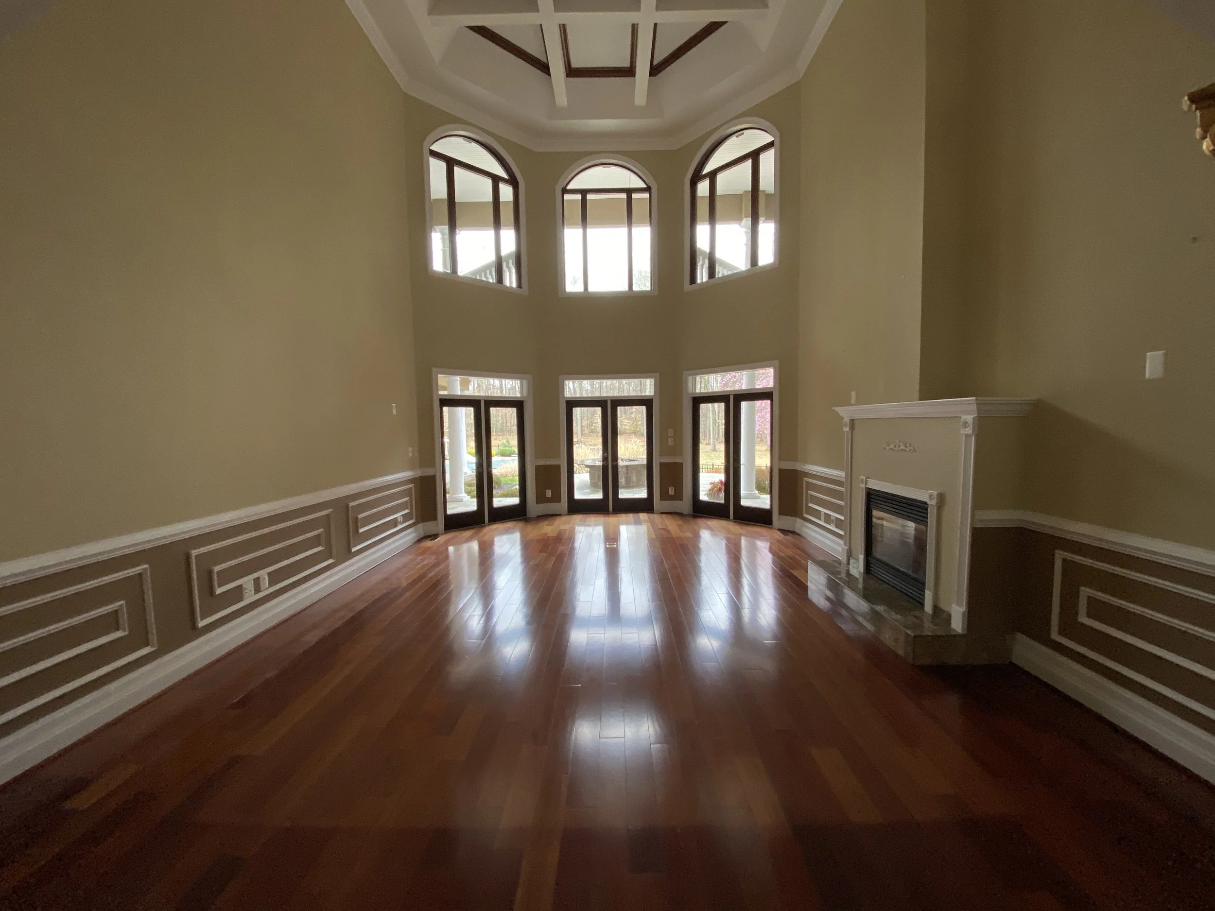 Empty living room with large windows, hardwood floor, and a fireplace.