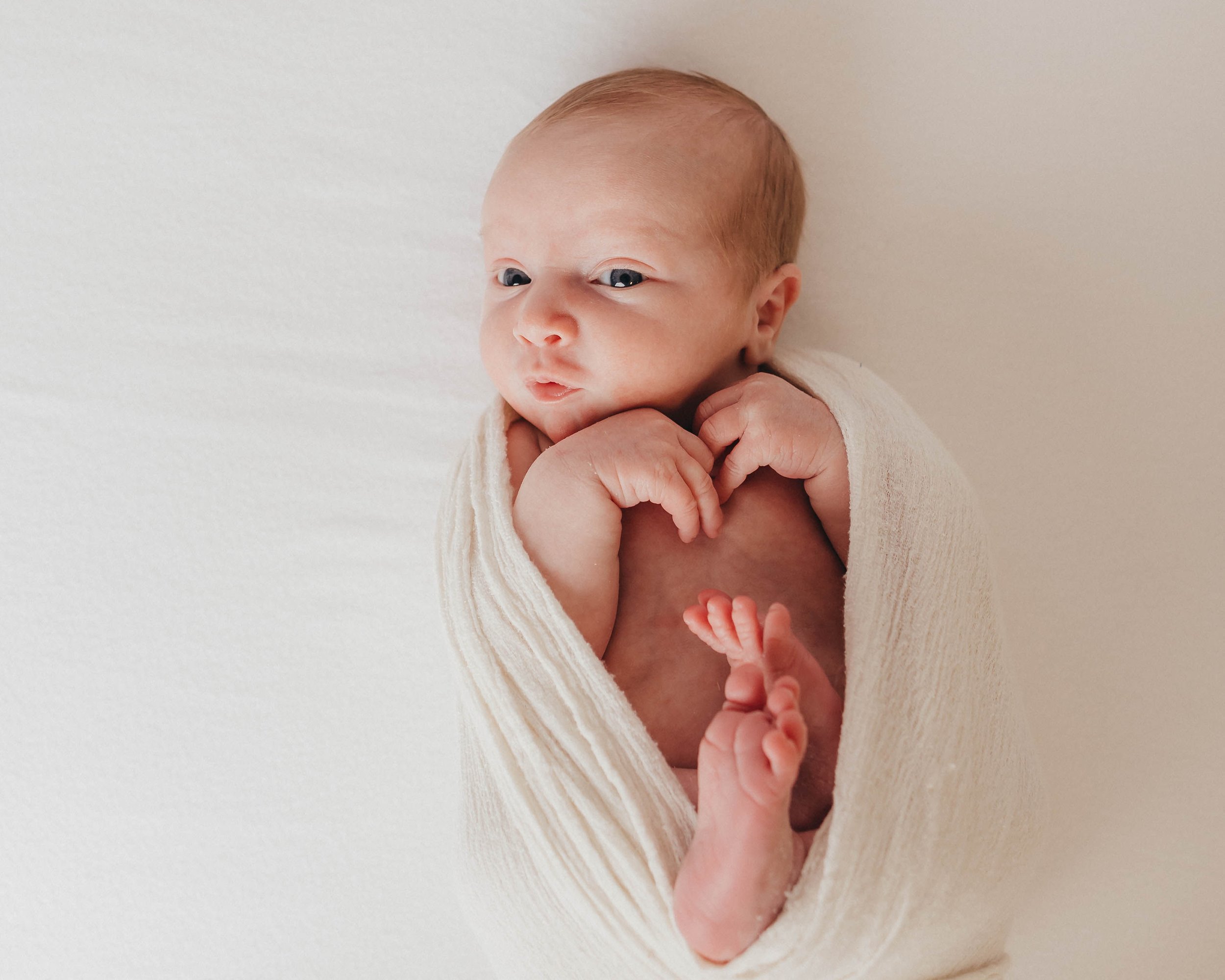 A sleeping baby wrapped in a yellow knitted blanket, lying on a woven basket with white flowers nearby.