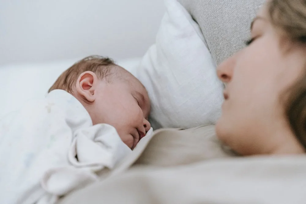 A mother and her newborn baby lying in bed, facing each other and sleeping