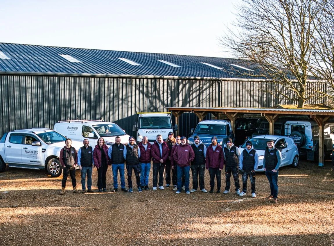 Group of people standing in front of company vehicles outside a warehouse