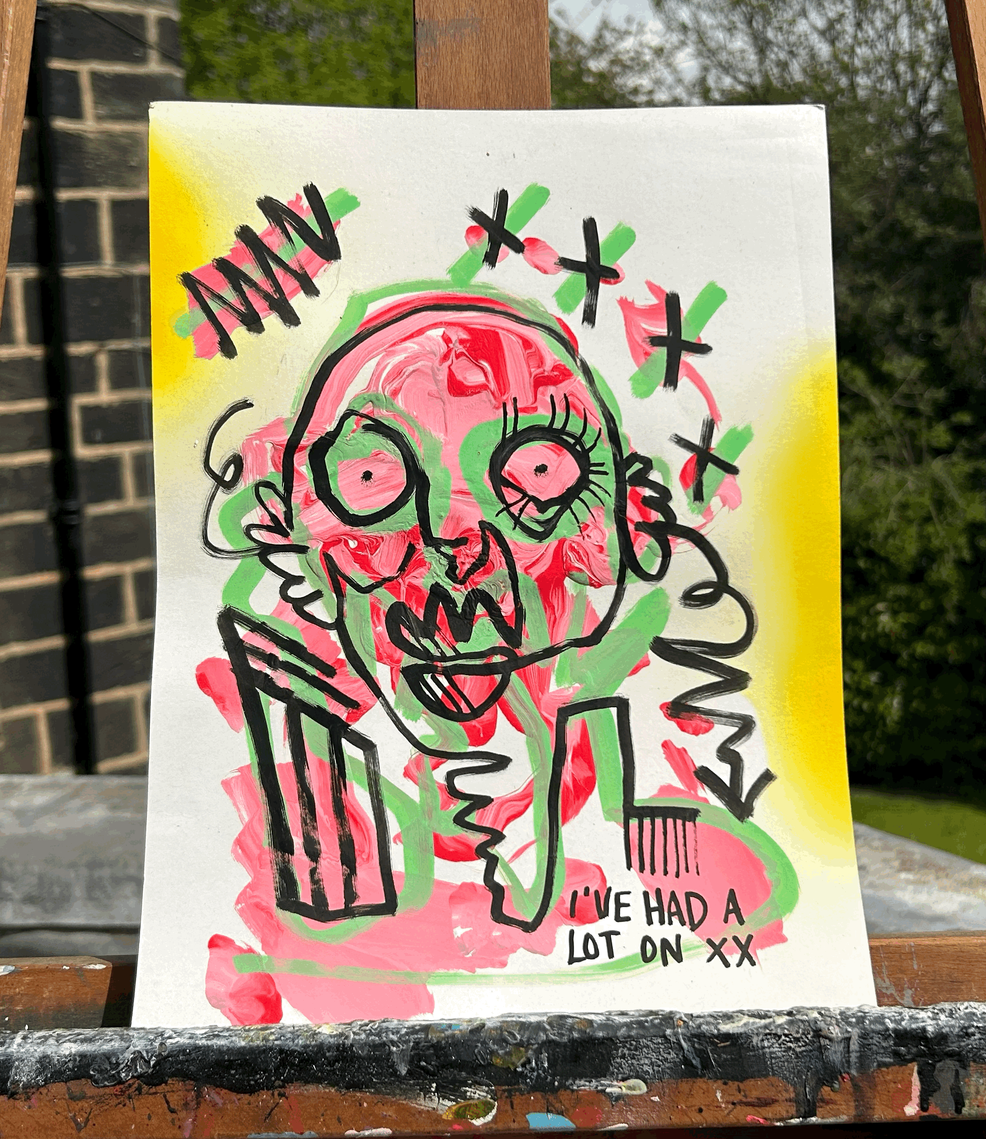 An abstract, colorful painting of a skull with exaggerated features, surrounded by green, pink, and red smudges. The skull has large, spiral eyes and an open mouth with a knife and a fork crossed behind it. Black graffiti-style text says 'ANNA' at th