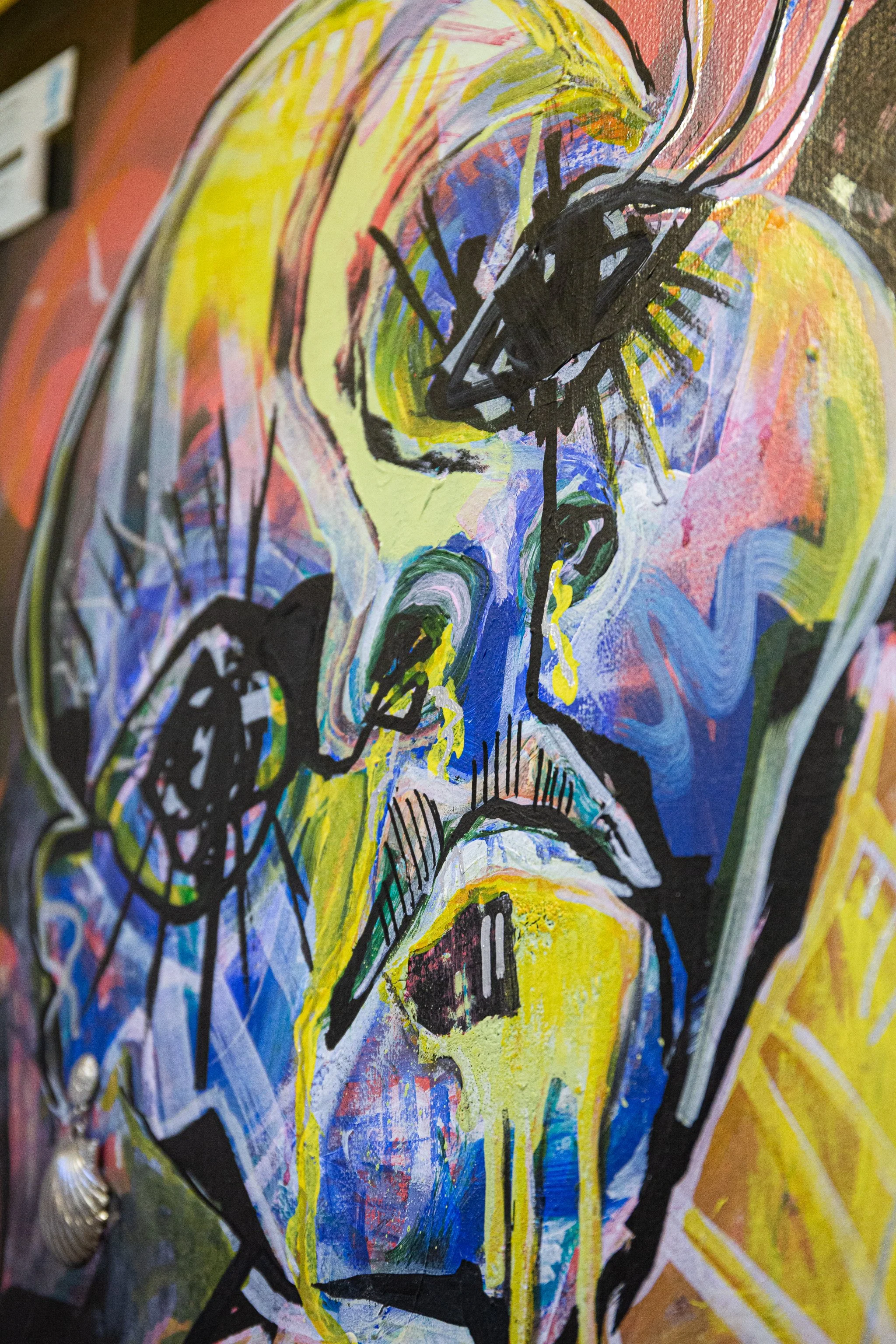 Abstract colorful painting of a person's face with expressive lines and splashes of paint, featuring prominent black lines and vibrant hues of yellow, blue, pink, and green.