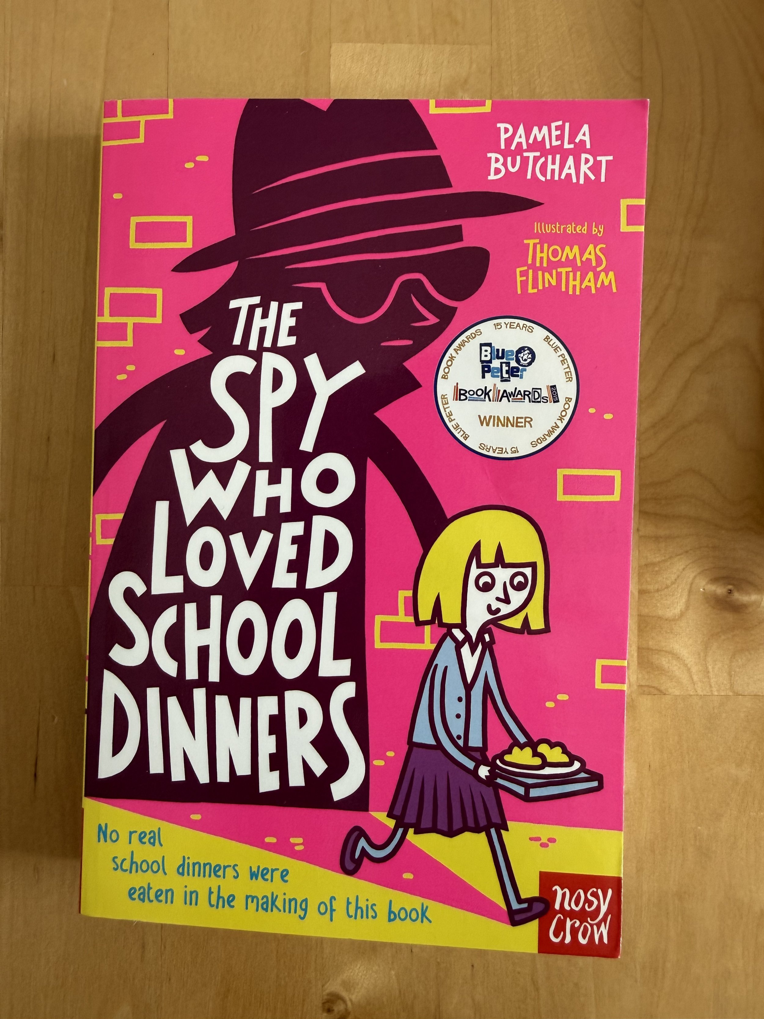 Cover of a children's book titled 'The Spy Who Loved School Dinners' by Pamela Butchart, illustrated by Thomas Flintham, featuring a stylized drawing of a girl in a hat and sunglasses with a plate of food.