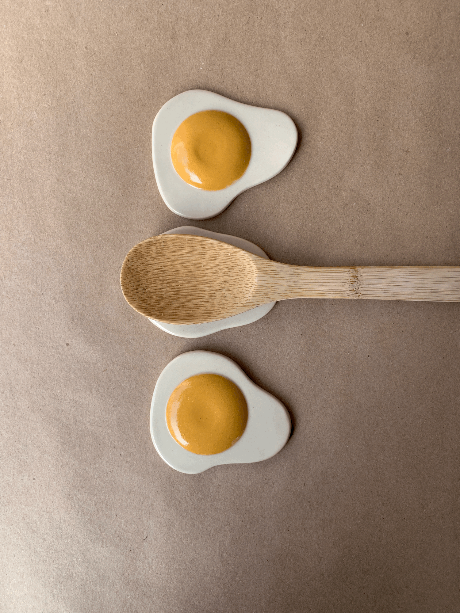 Fried Egg Spoon Rests, two egg-shaped ceramic spoon rests with a wooden spoon