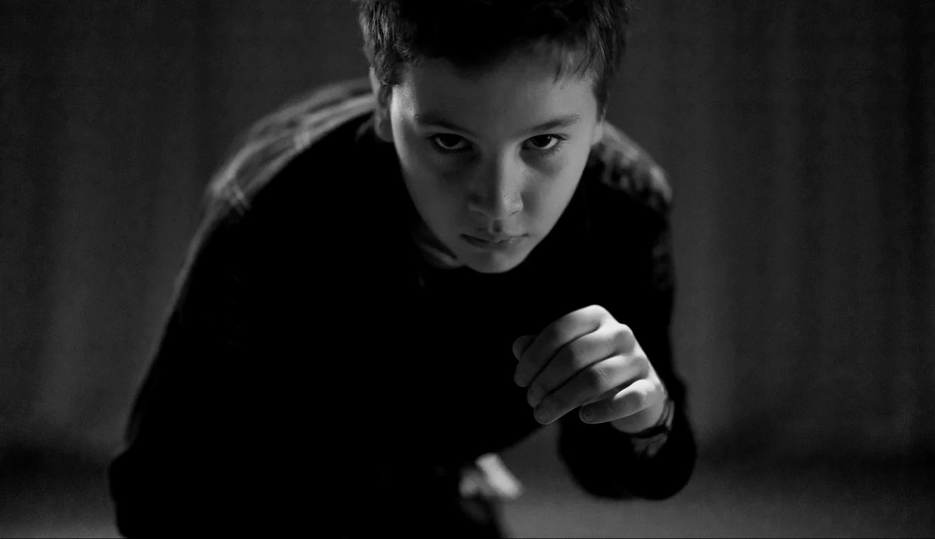 A young boy looks at the camera in a defensive mma position