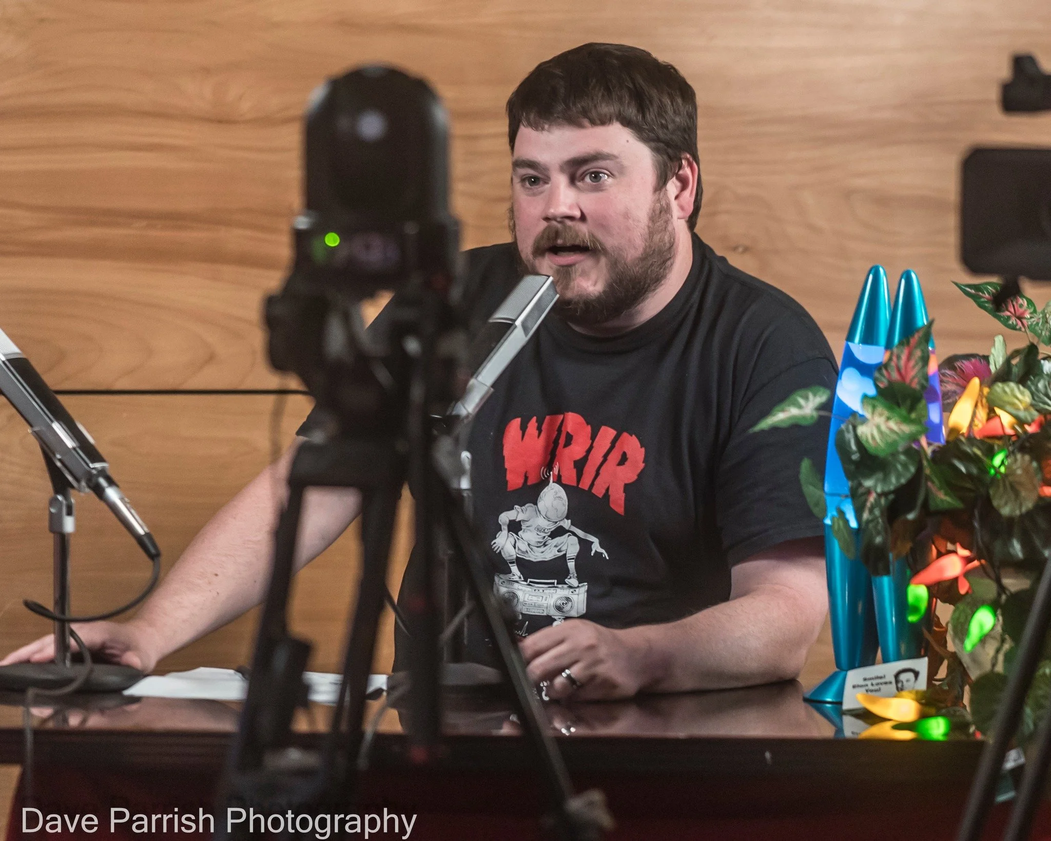 A man sitting behind a desk, speaking into a microphone.