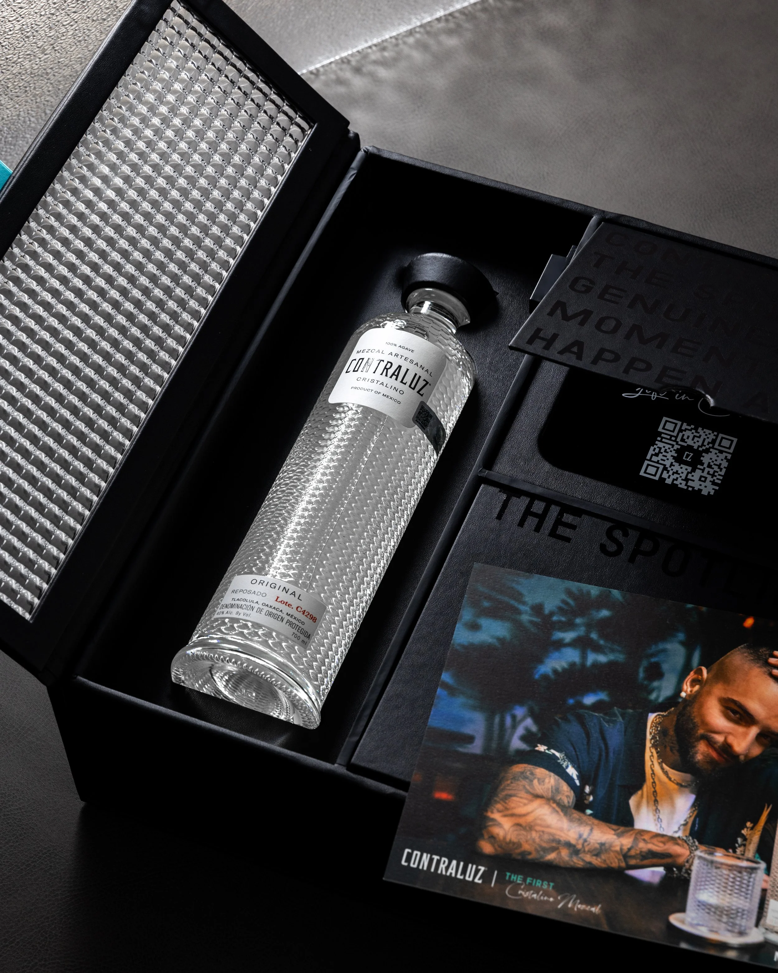 A bottle of Contraluz mezcal in a textured package, accompanied by promotional materials and a picture of a man.