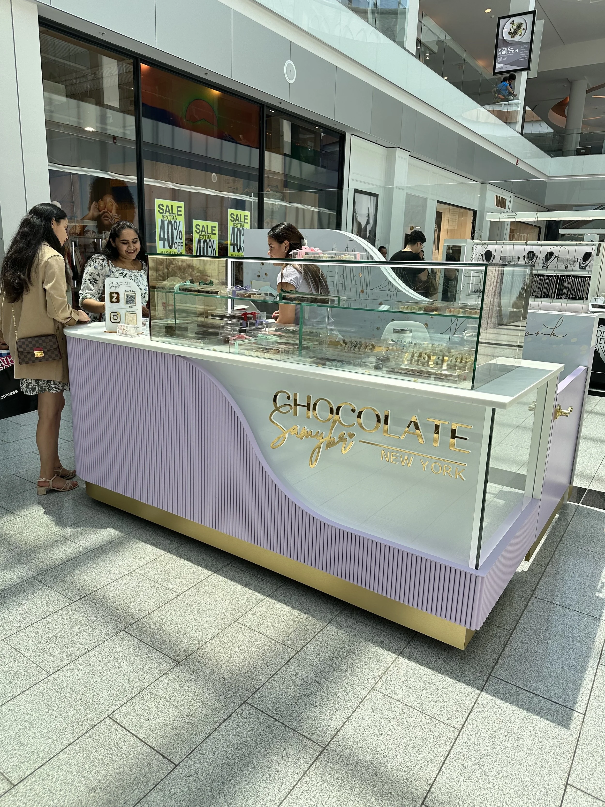 A custom made chocolate letters kiosk in a shopping mall Roosevelt Field, Garden City, NY. The kiosk has a sign that says 'Chocolate Samybri New York'.