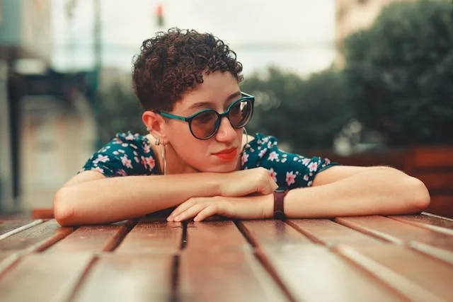 A woman overwhelmed and leaning on a table with sunglasses on