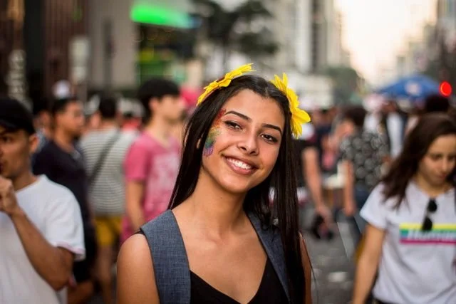 A woman in a crowded street with rainbow glitter on her face