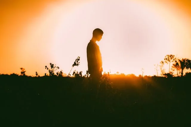 A person standing alone with the sunrise behind them