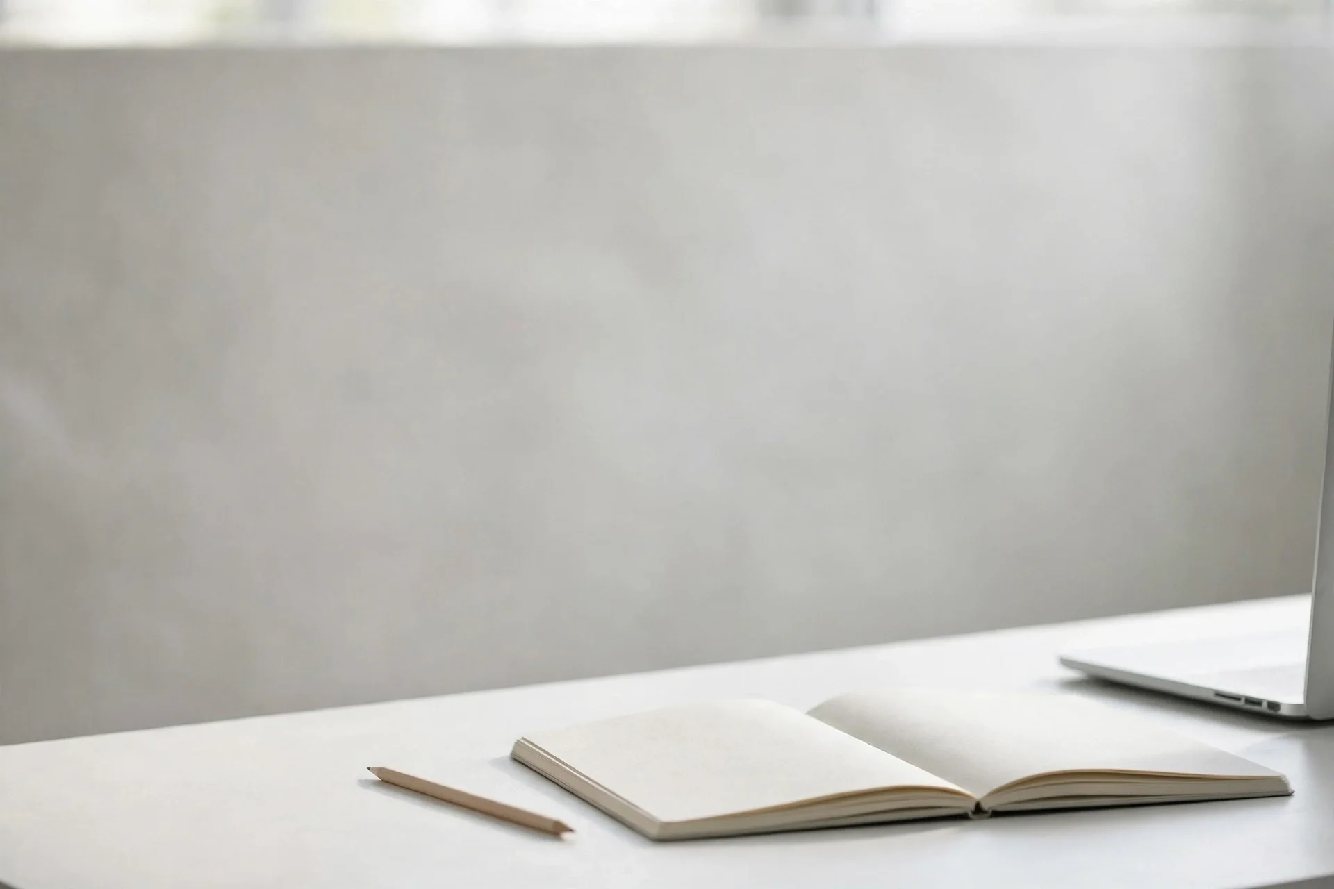 Minimal white desk workspace with an open notebook, pencil, and laptop edge