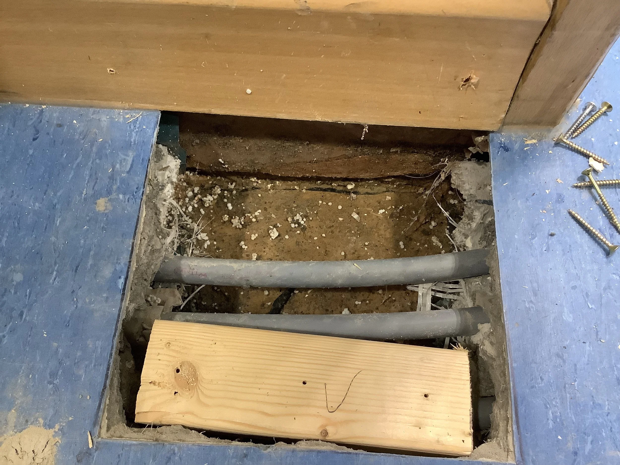 Trial hole beneath floor showing underfloor heating conduits and concrete substrate where moisture tracking between DPC and DPM was confirmed – Durndell Building Surveyors, Milton Keynes.