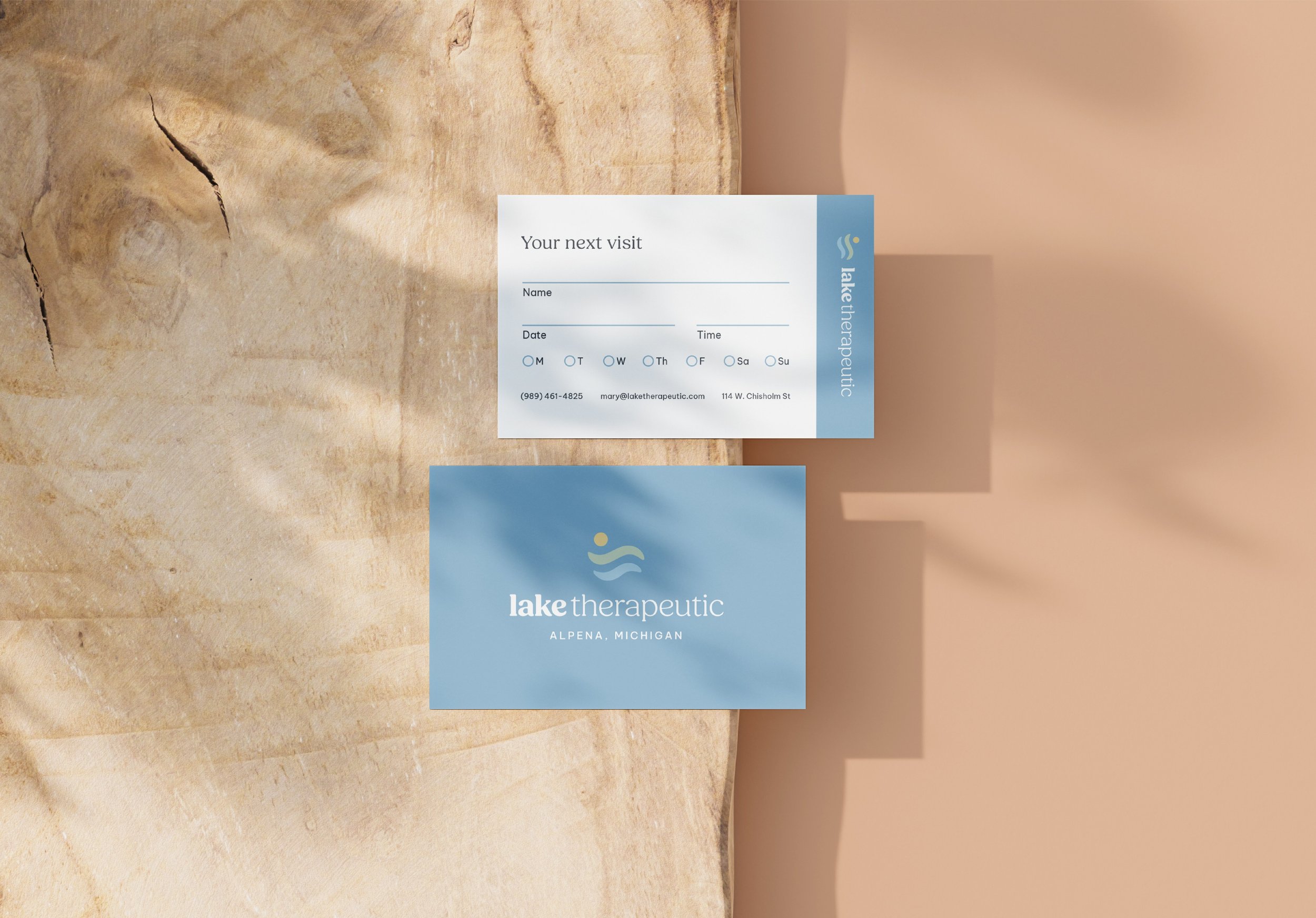 A business card and an appointment slip for Lake Therapeutic in Alpena, Michigan are placed on a marble surface. The appointment slip is for a future visit and includes fields for name, date, and time, with days of the week options.