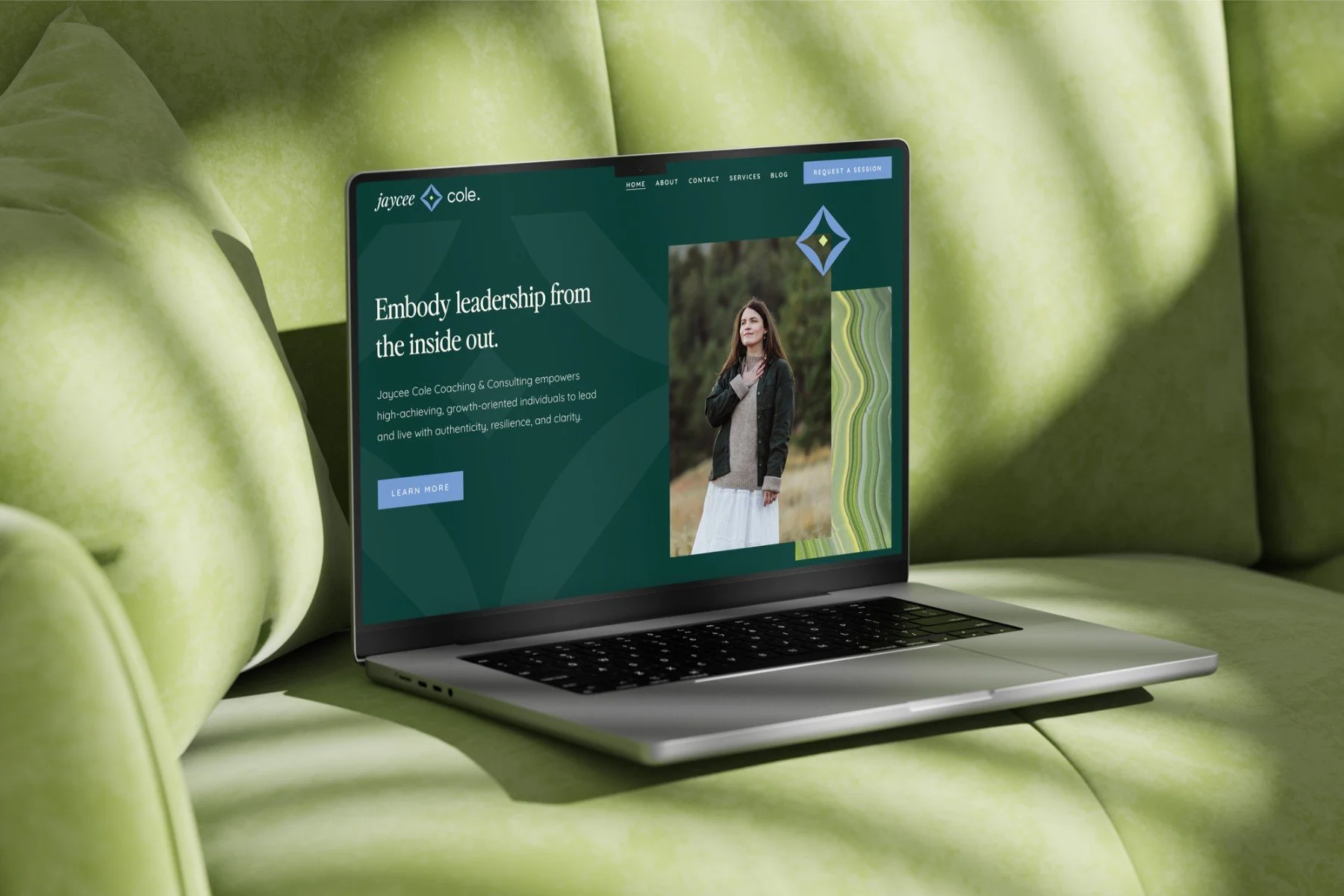 Laptop on green sofa displaying a coaching website with a woman outdoors, the website headline says 'Embody leadership from the inside out.'