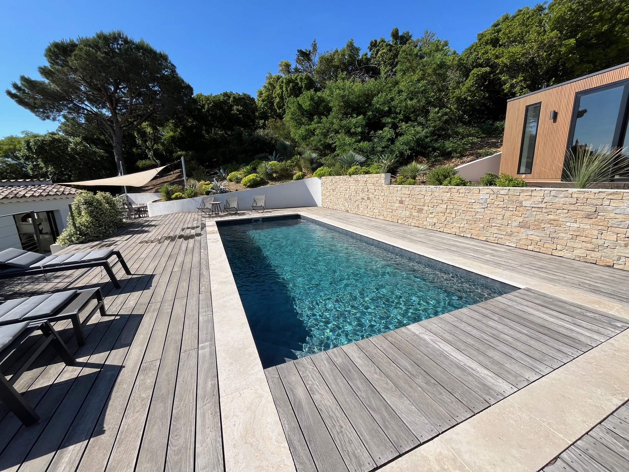 Vue panoramique depuis une terrasse avec mobilier de jardin en rotin, palmiers, mer et ciel bleu en arrière-plan.