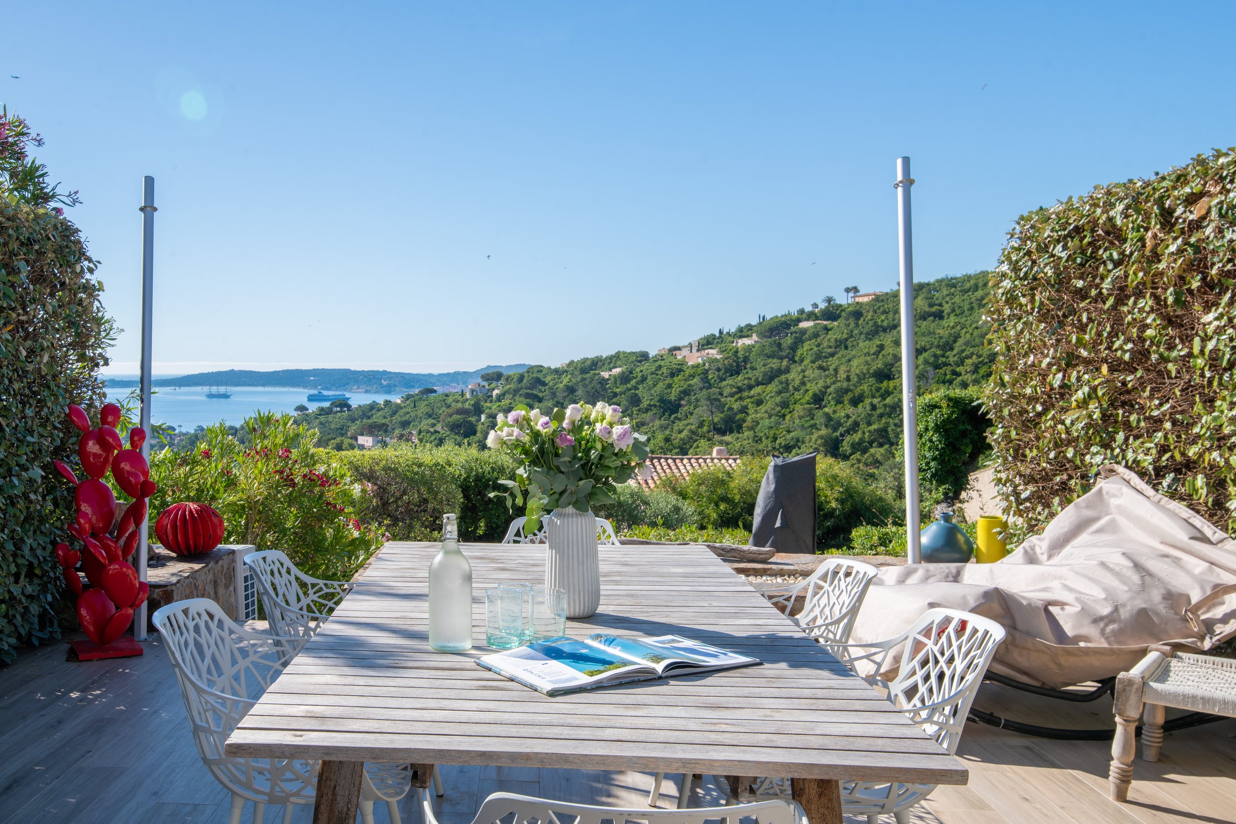 Paysage méditerranéen avec vue sur la mer, maisons, et collines verdoyantes sous un ciel bleu.