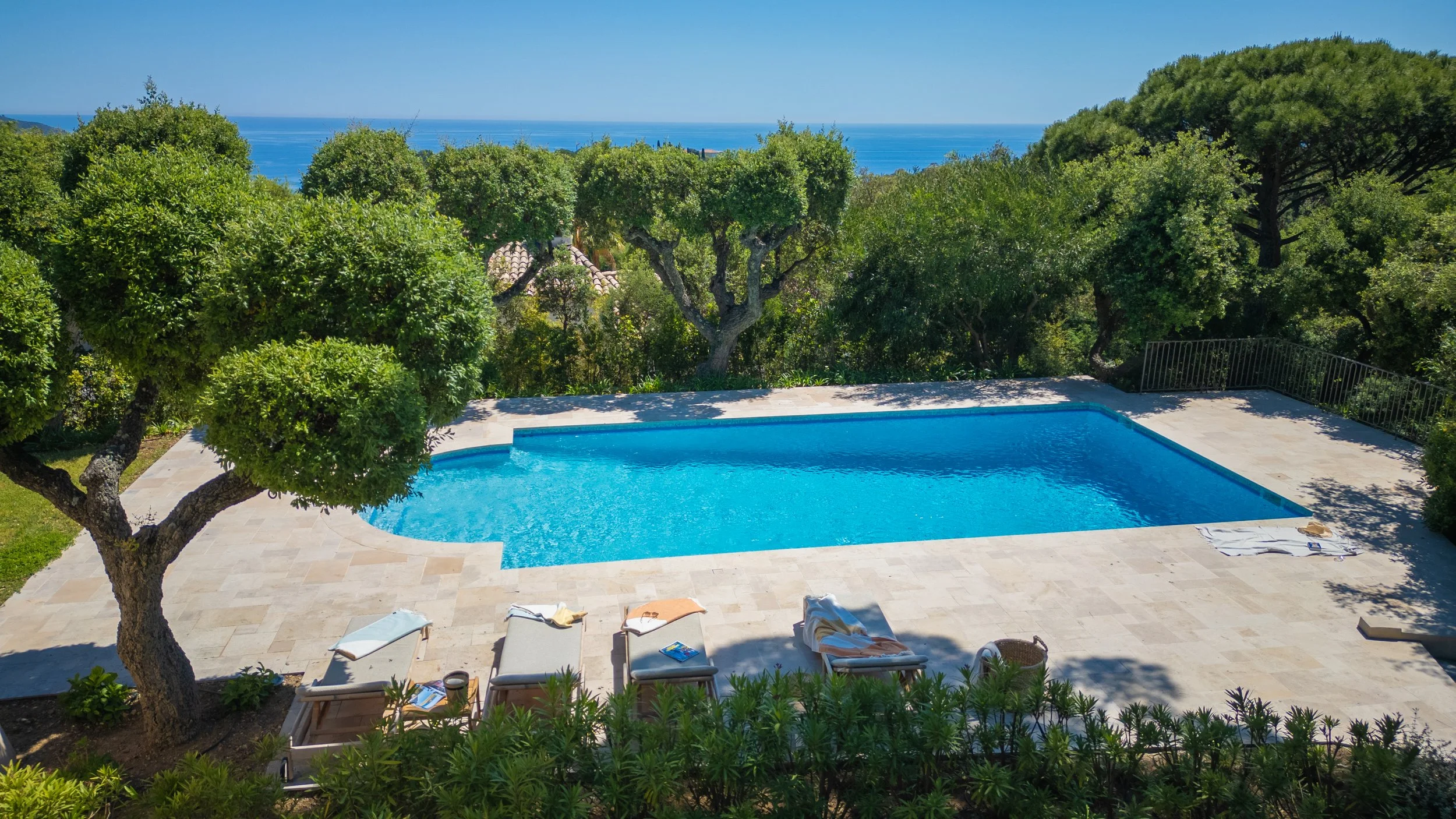 Piscine avec chaises longues et arbres en arrière-plan.
