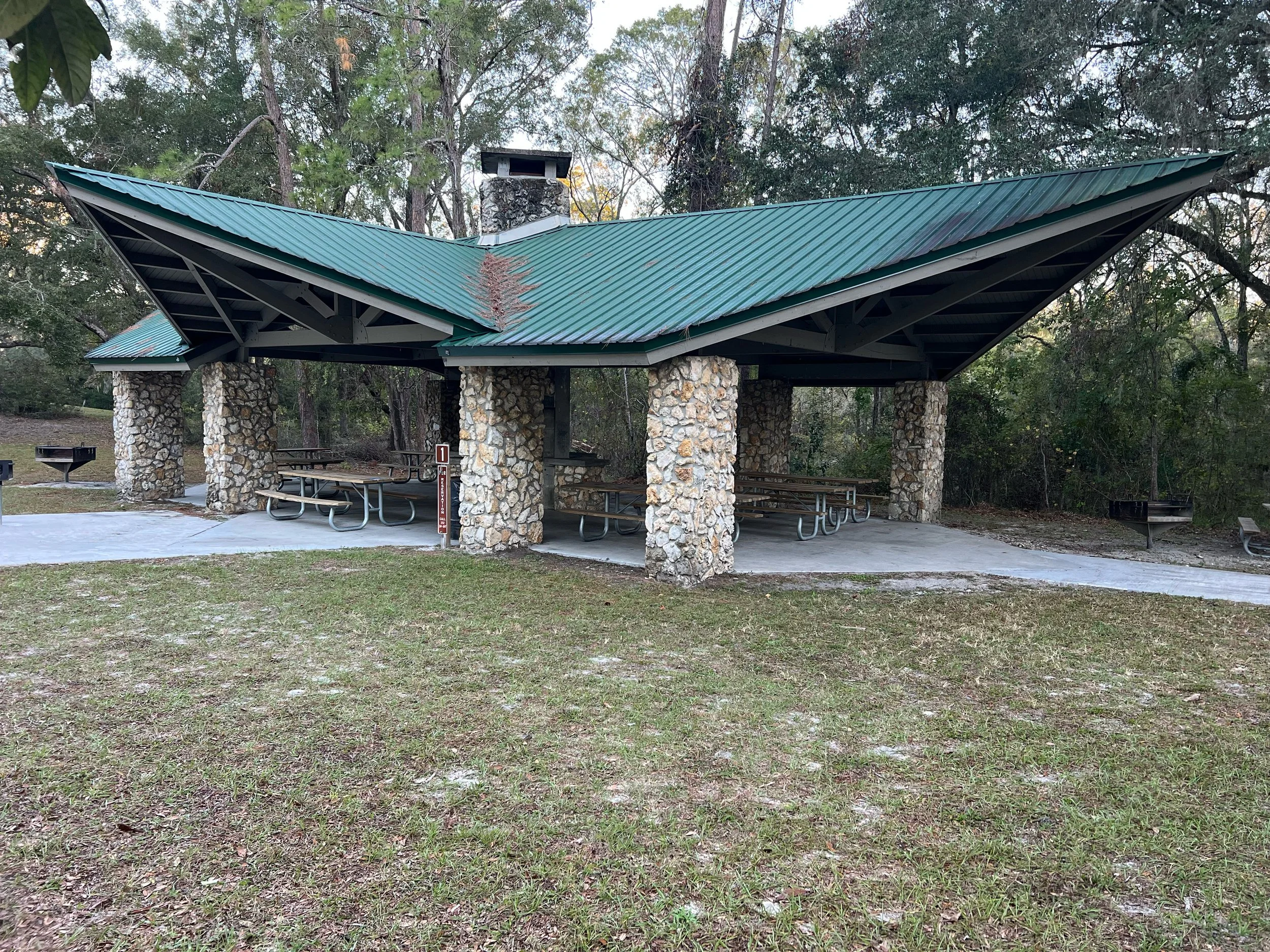 A large covered pavilion with picnic tables and a centered fireplace