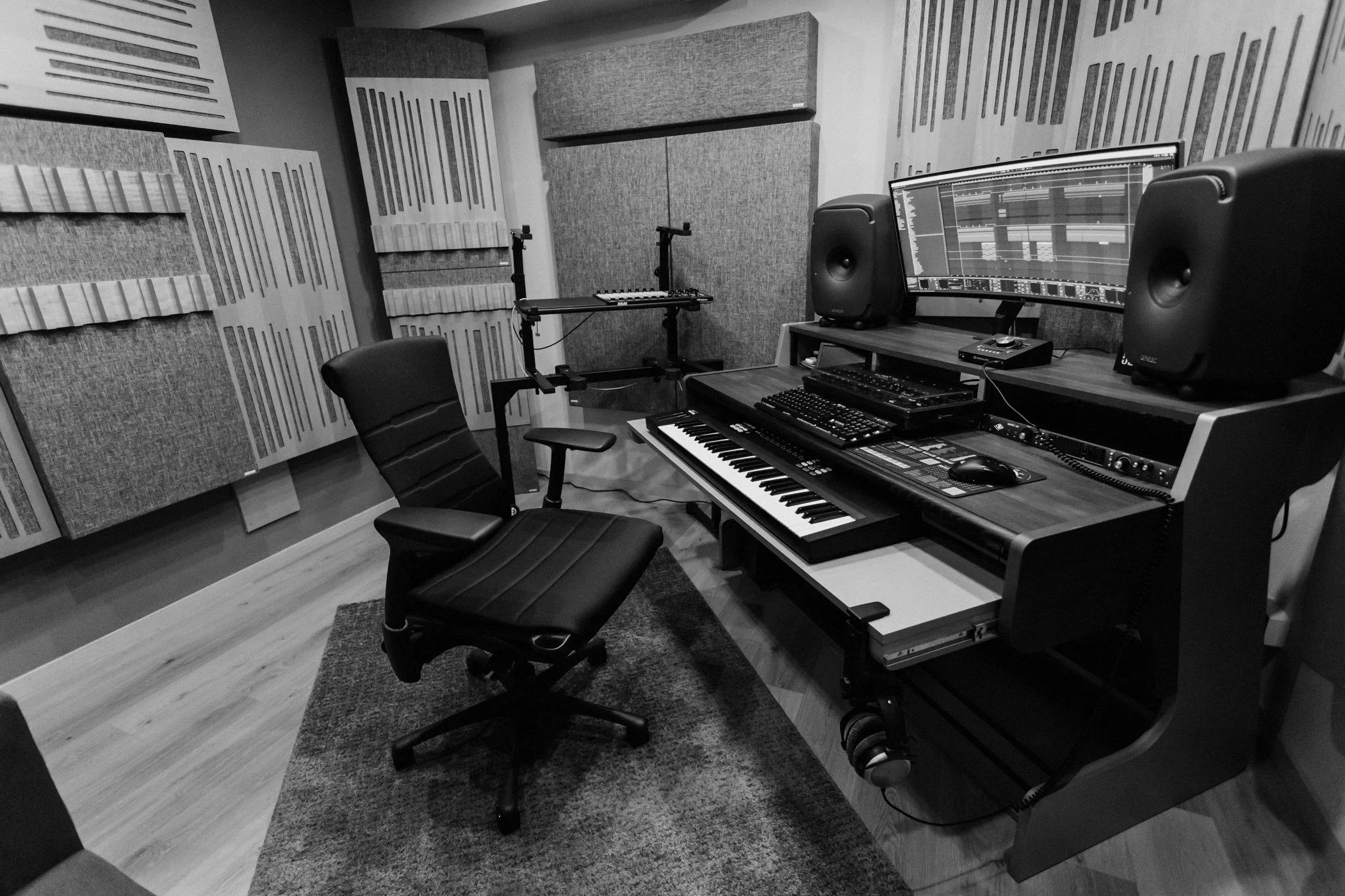 Matteo Tura's recording studio with soundproofed walls, a desk with a computer monitor displaying music editing software, two studio speakers, a digital keyboard, and various music production equipment.
