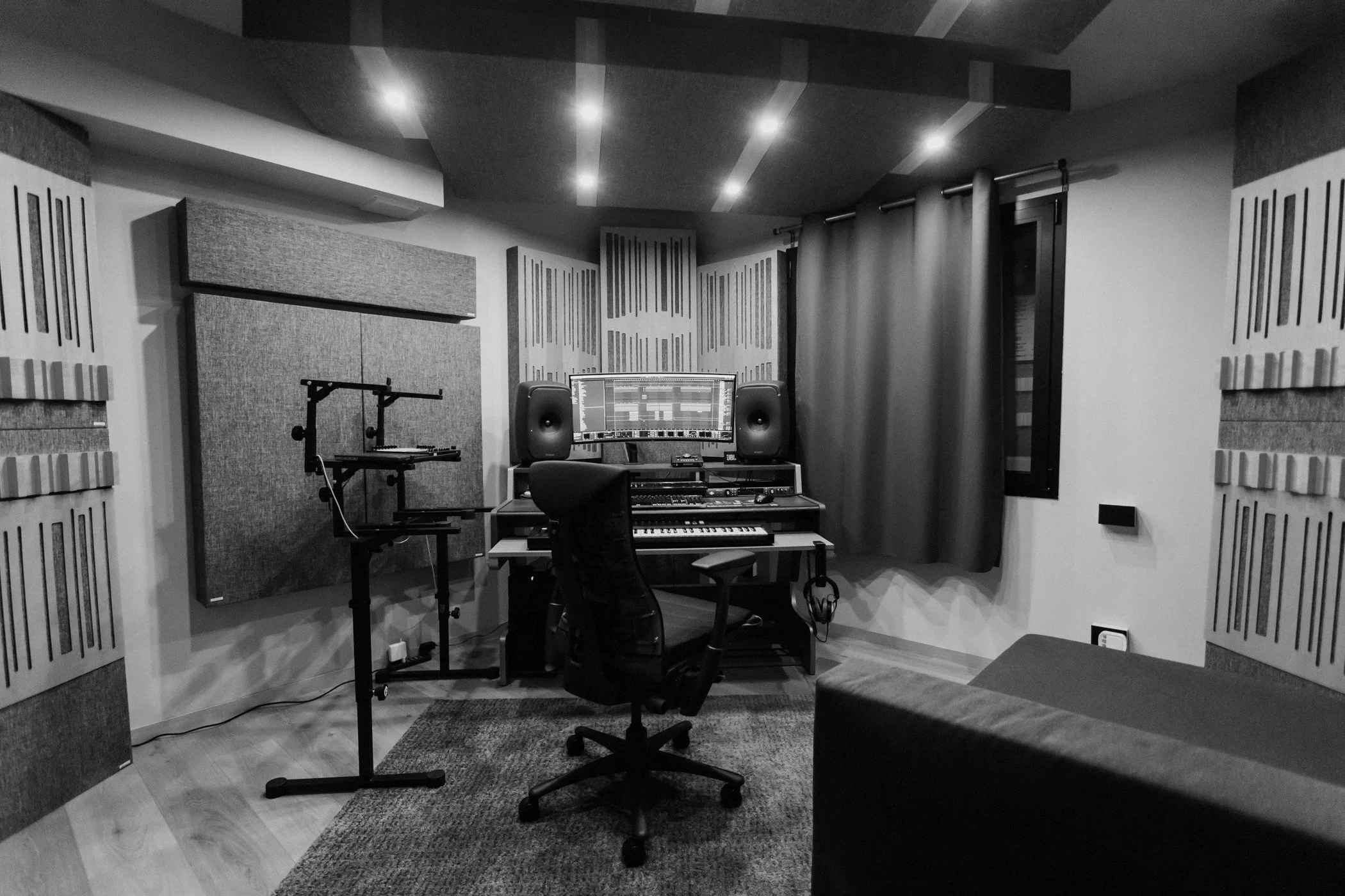 Matteo Tura's sound recording or music production studio with acoustic panels, a computer monitor displaying audio editing software, studio speakers, a keyboard, and a chair, all in black and white.