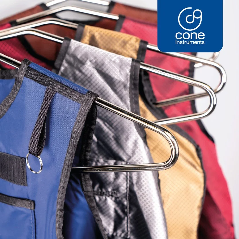 Multiple colorful backpacks hanging on metal racks with a Cone Instruments logo in the top right corner.