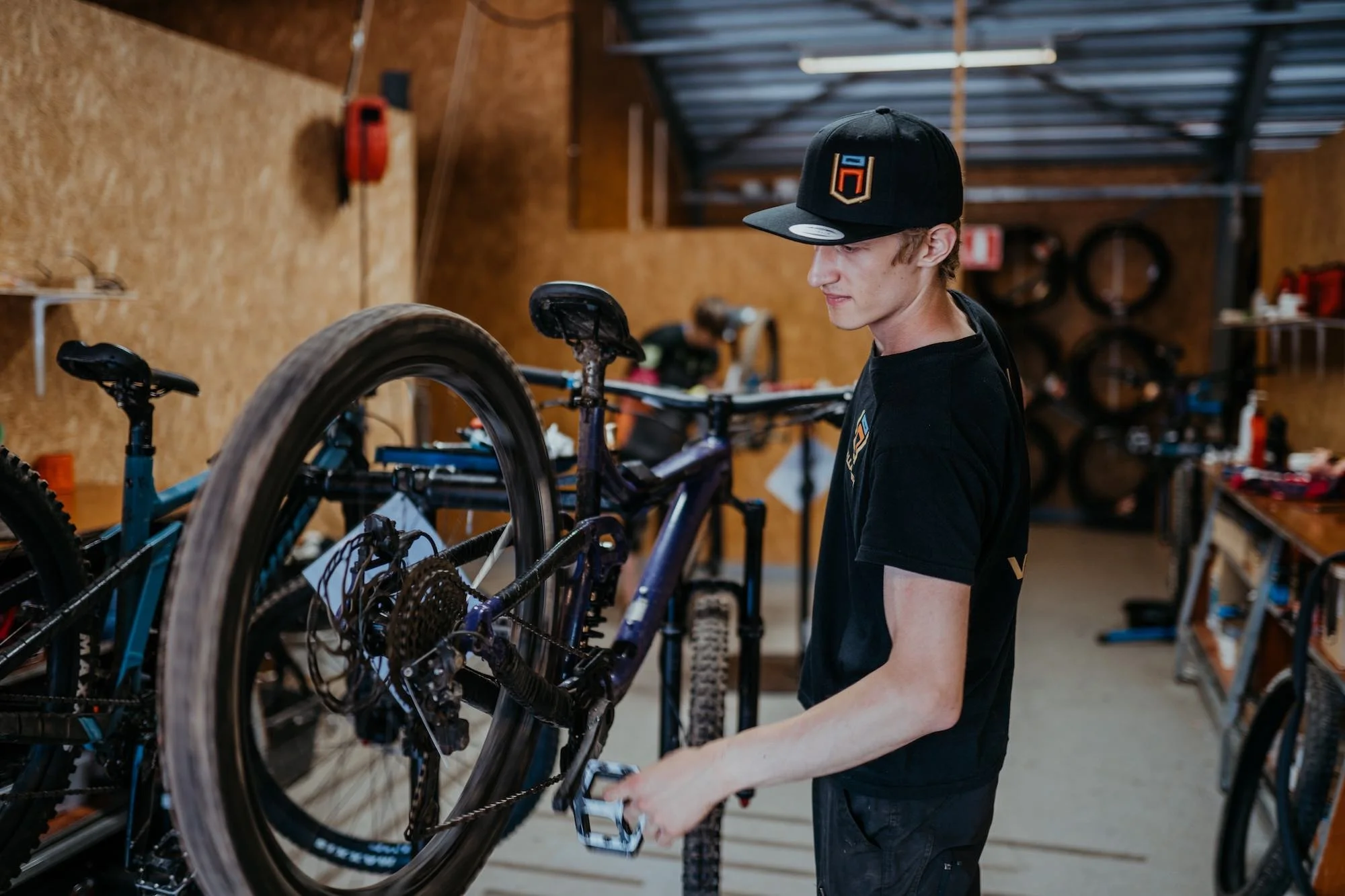 En man i svart t-shirt och svart keps som underhåller en mtb i en cykelverkstad.