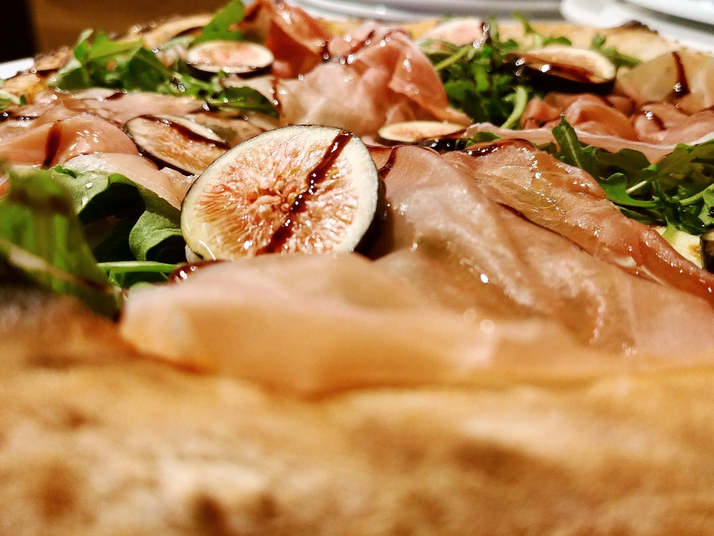 Close-up of a pizza with arugula, figs, prosciutto, and balsamic glaze.