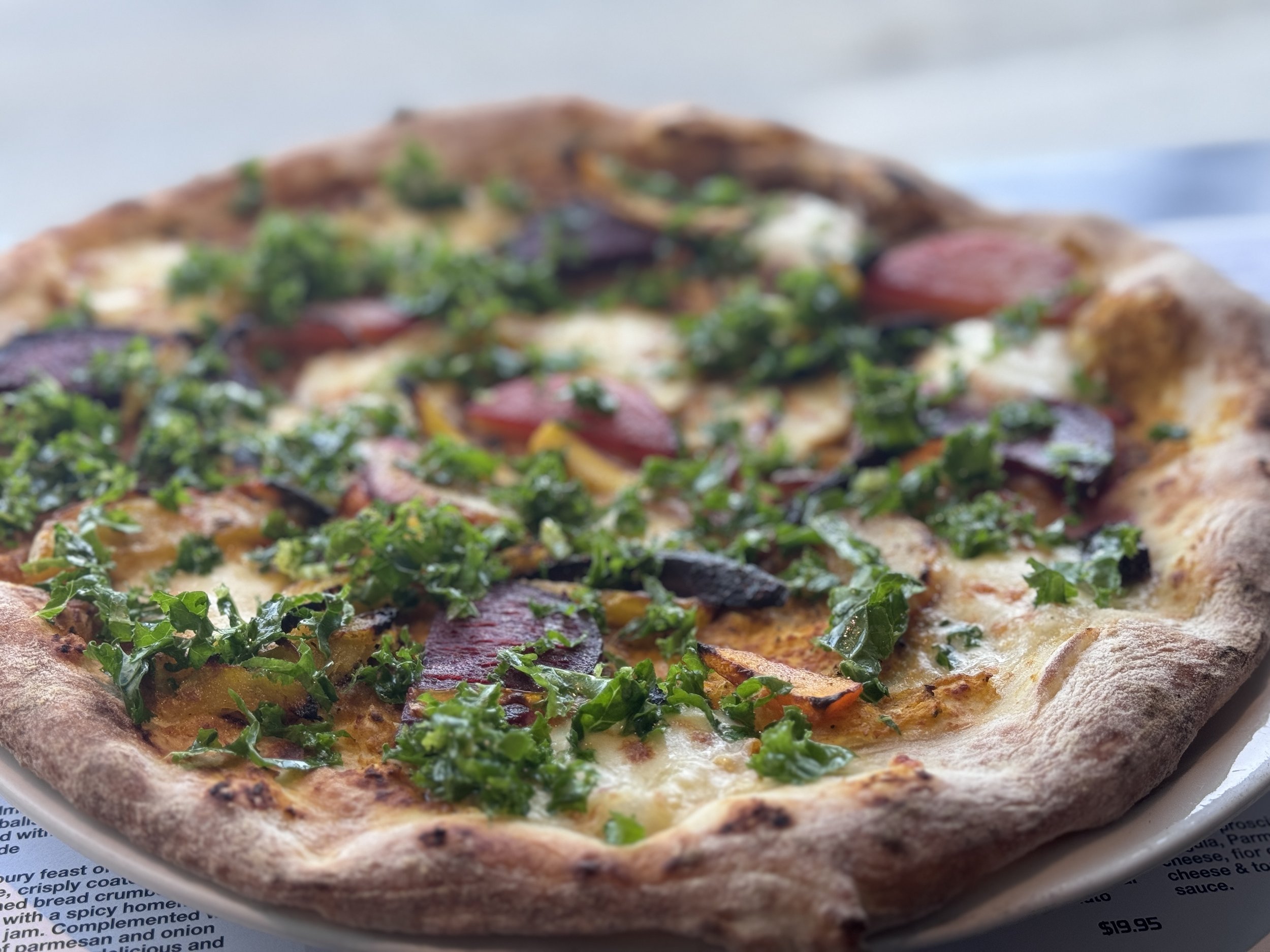 Close-up of a decorated pizza with greens, sliced sausage, and vegetables on a crust.