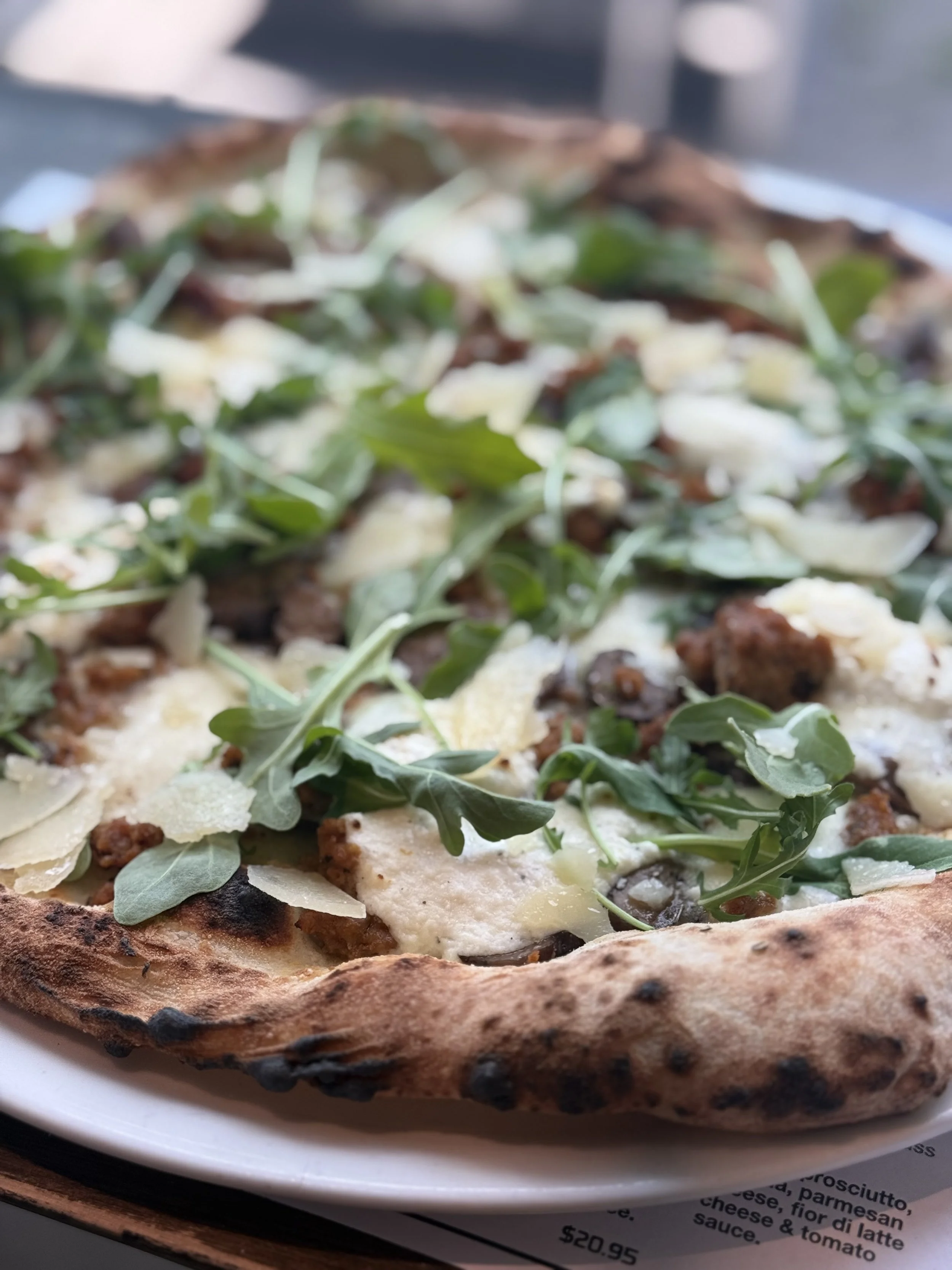 Close-up of a pizza topped with fresh arugula, cheese, and pieces of sausage on a white plate.