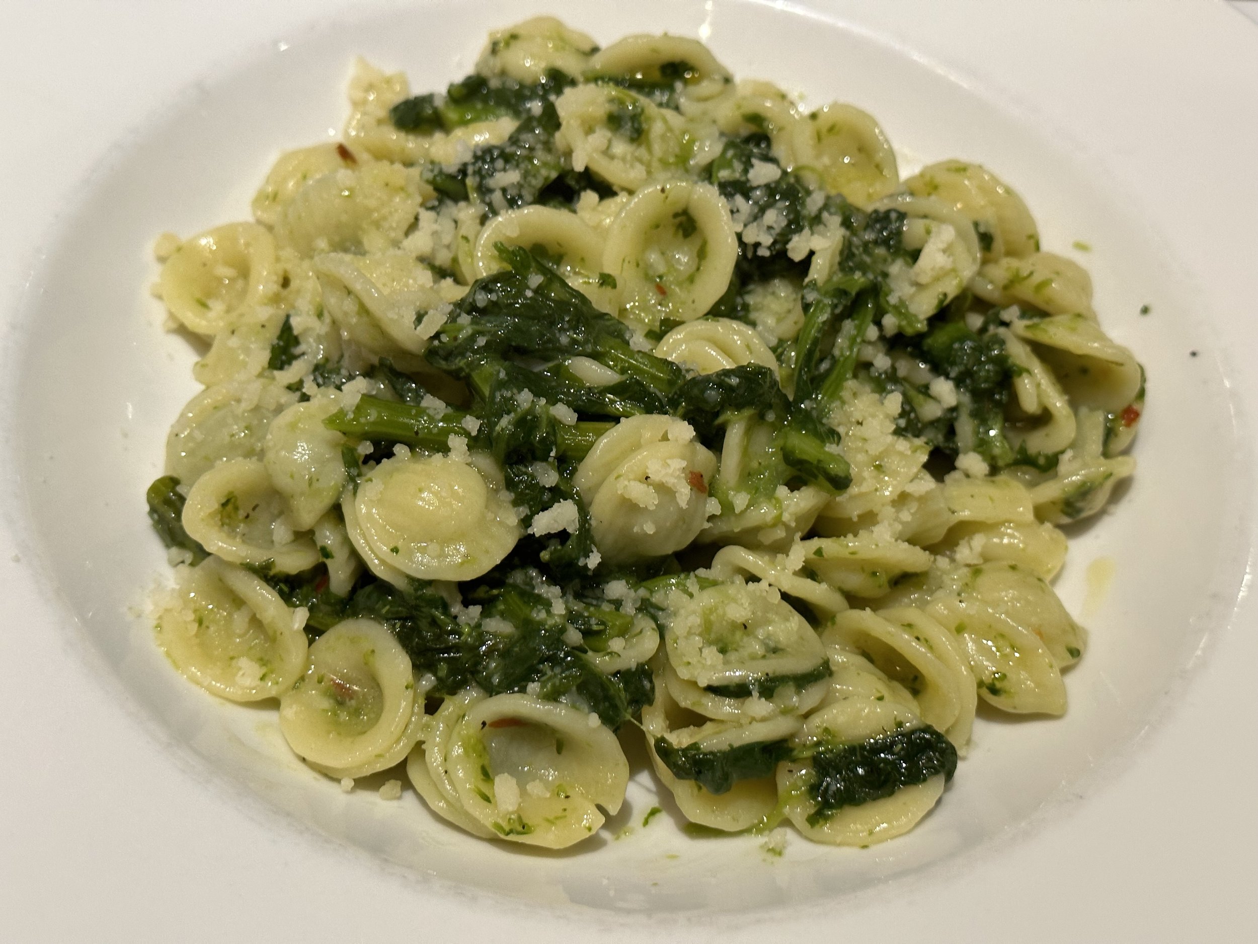 Plate of orecchiette pasta with chopped spinach and grated cheese.